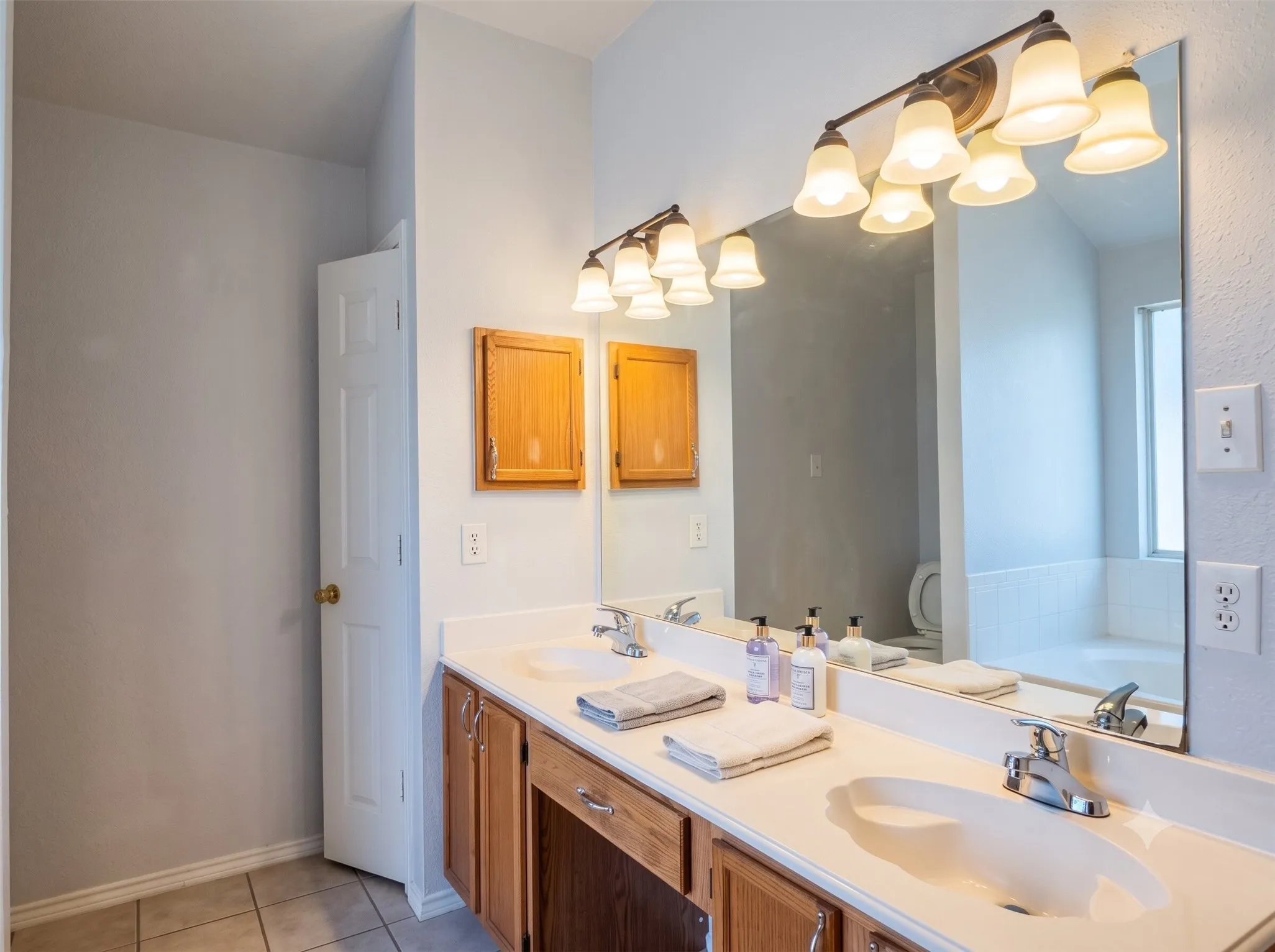 Dual vanity with integrated sinks, wood-finish cabinetry, and a large wall-mounted mirror