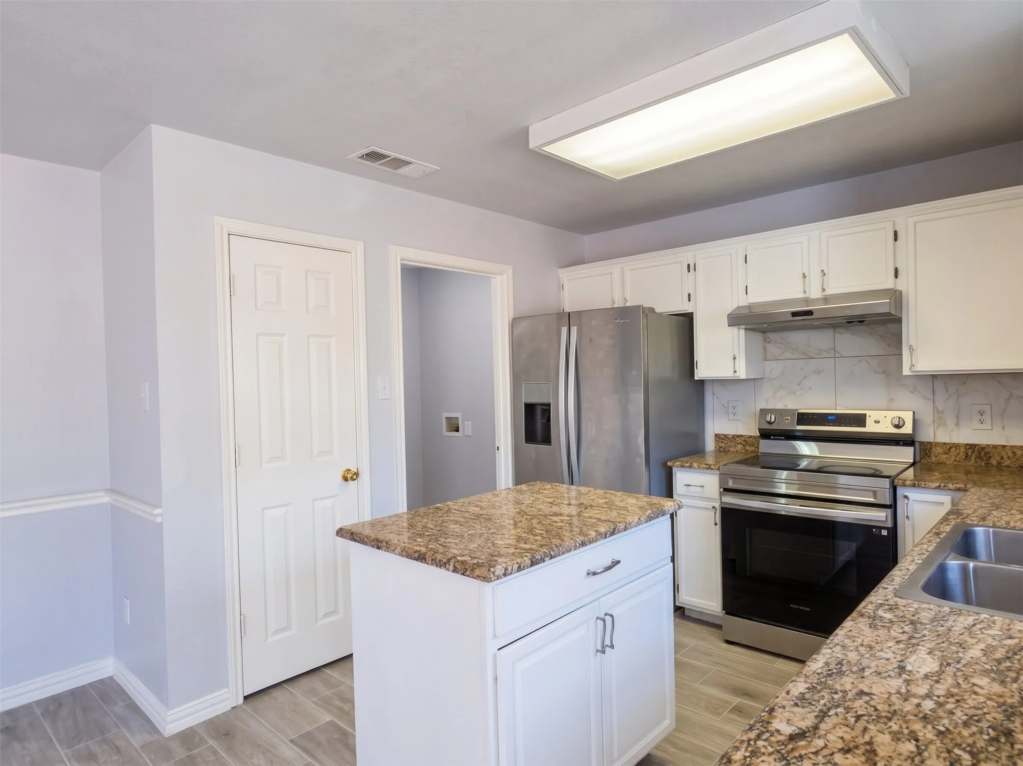 Kitchen featuring white cabinetry, granite-style countertops, stainless steel appliances, a center island, and wood-finish​​‌​​​​‌​​‌‌​‌‌​​​‌‌​‌​‌​‌​​​‌​​ flooring