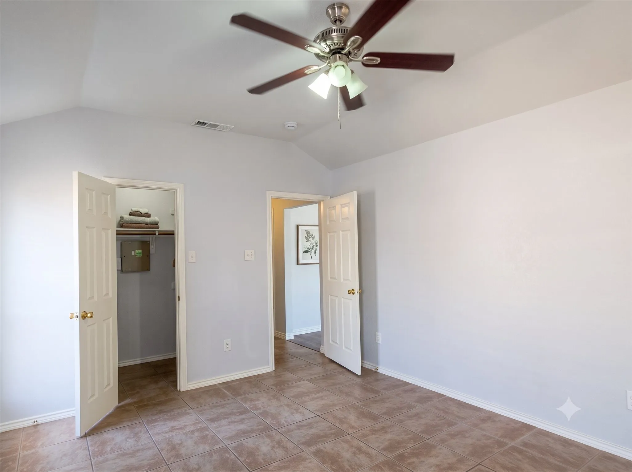 Vaulted ceiling, ceiling fan with integrated lighting, tiled flooring, built-in closet with shelving, and paneled interior doors