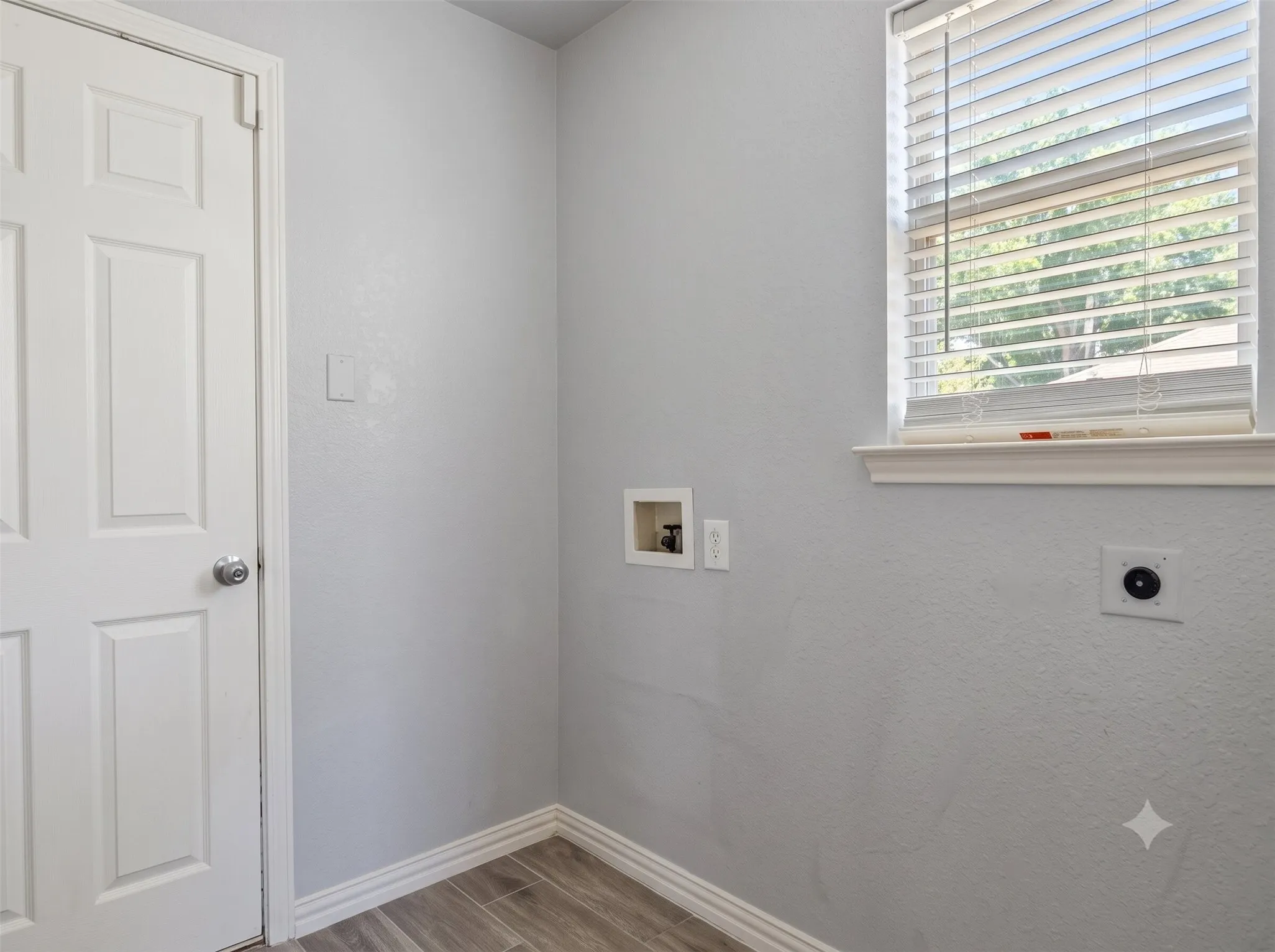 Light gray wall finish, window with white blinds, wood-finish flooring, white baseboards, and a white paneled door