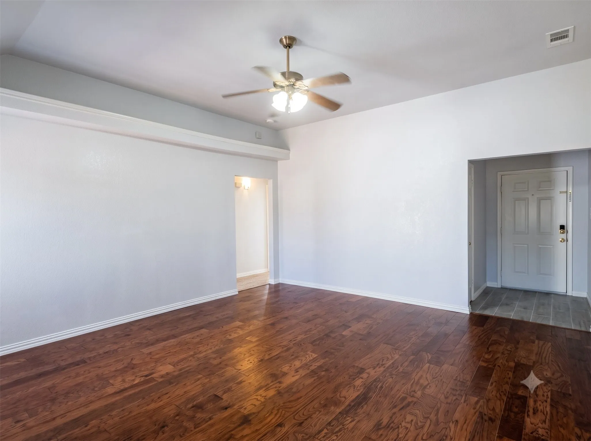 Hardwood-style flooring throughout, ceiling fan with integrated lighting, recessed entryway with tile flooring, and neutral wall paint