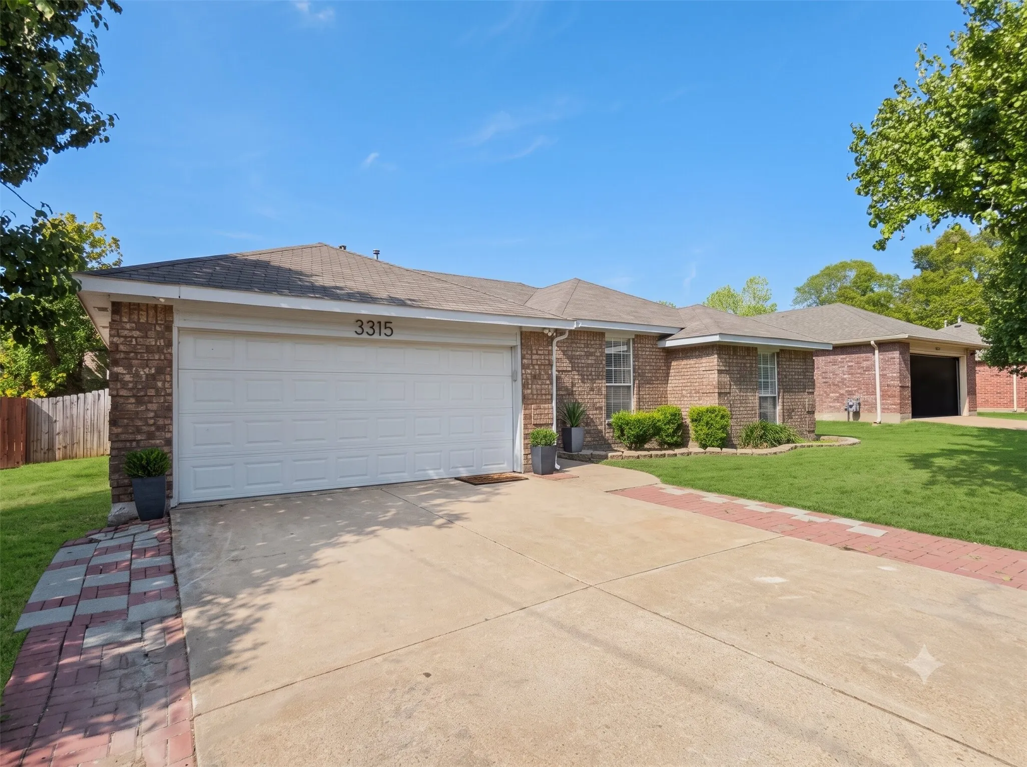 Brick exterior with a white garage door, concrete driveway, and red paver accents