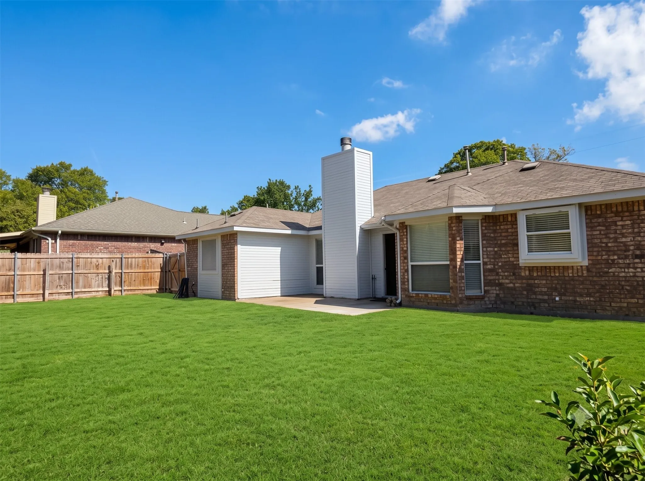 Expansive backyard with a manicured lawn, brick exterior, and a wood privacy fence