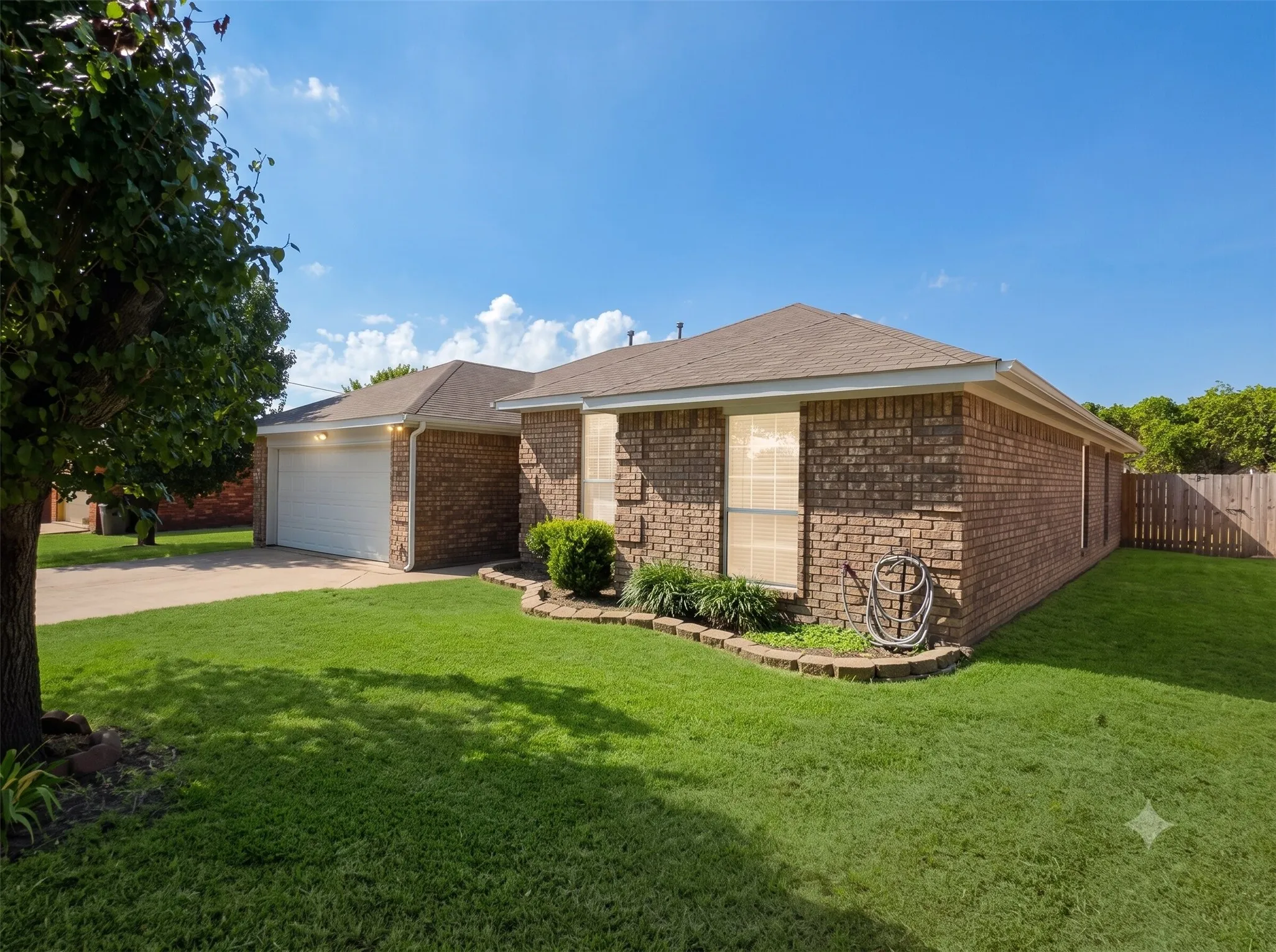Brick exterior, attached garage, well-maintained lawn, privacy fence, and mature landscaping