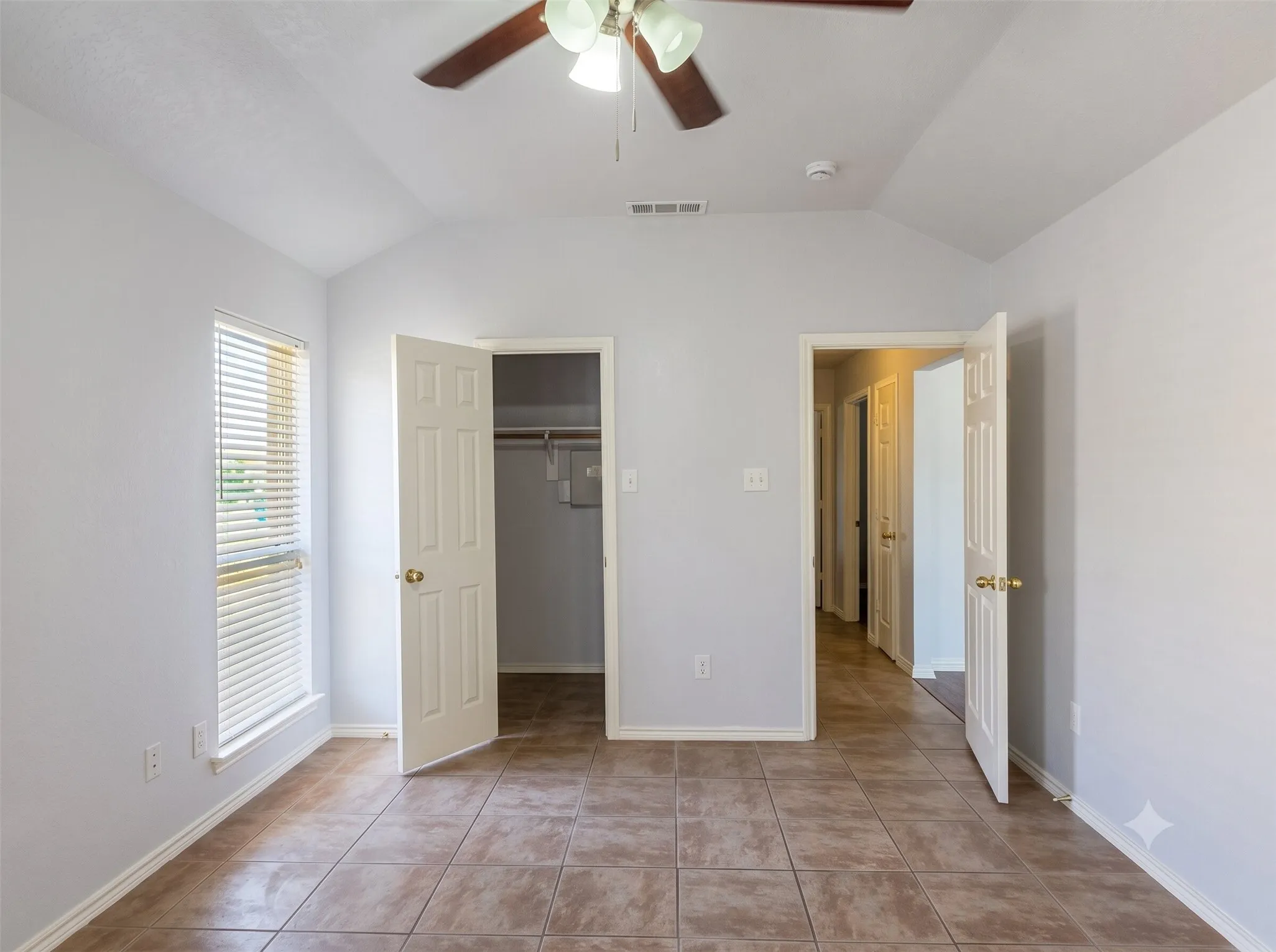 Vaulted ceiling with a ceiling fan, tiled flooring, window with blinds, and paneled doors