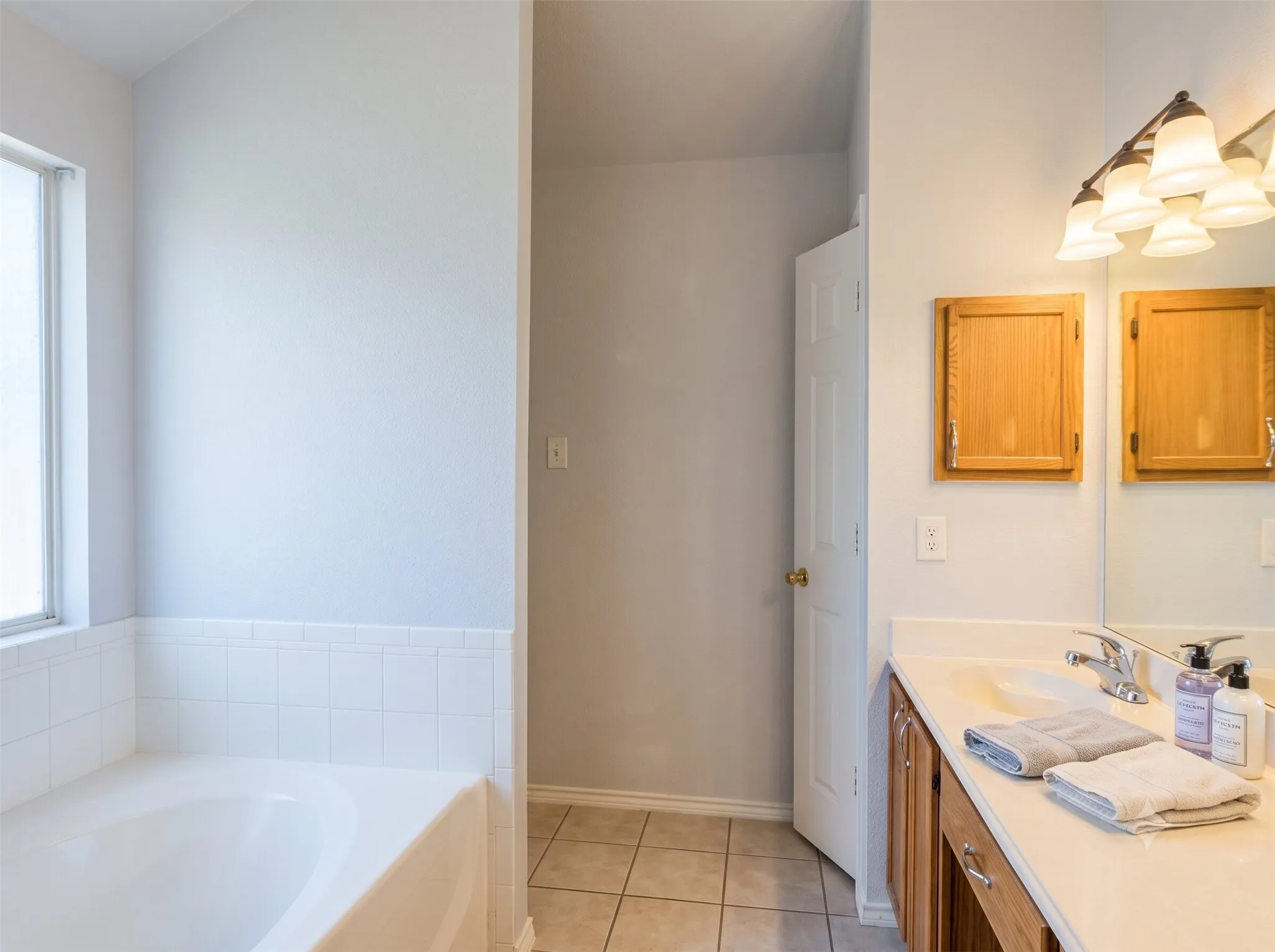 Built-in bathtub with white tile surround, dual wood-finish medicine cabinets, single vanity with integrated sink, and tile flooring