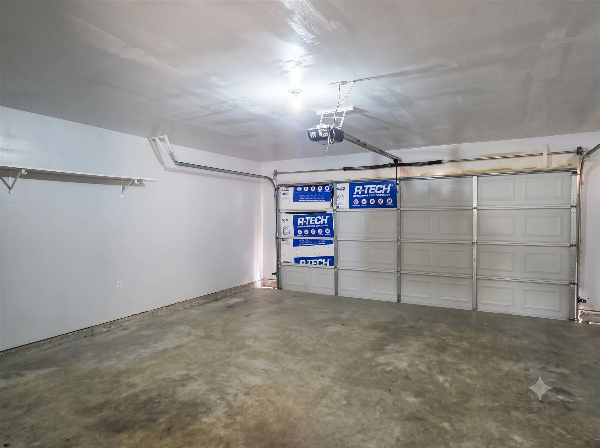 Garage interior featuring a concrete floor, white painted walls, built-in shelving, and an automatic garage door opener