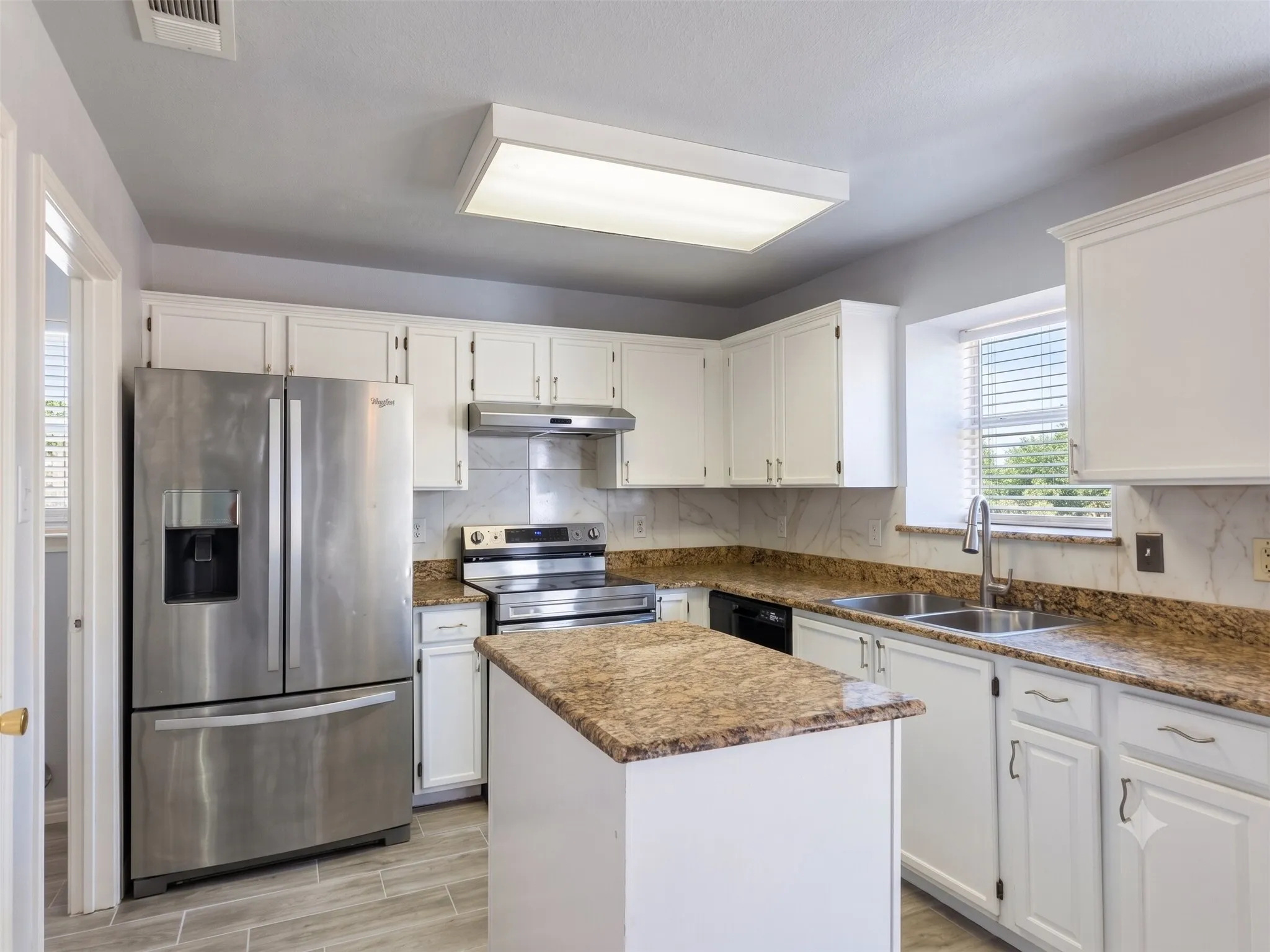 Kitchen featuring white cabinetry, granite-finish countertops, stainless steel appliances, a center island, and wood-finish tile flooring