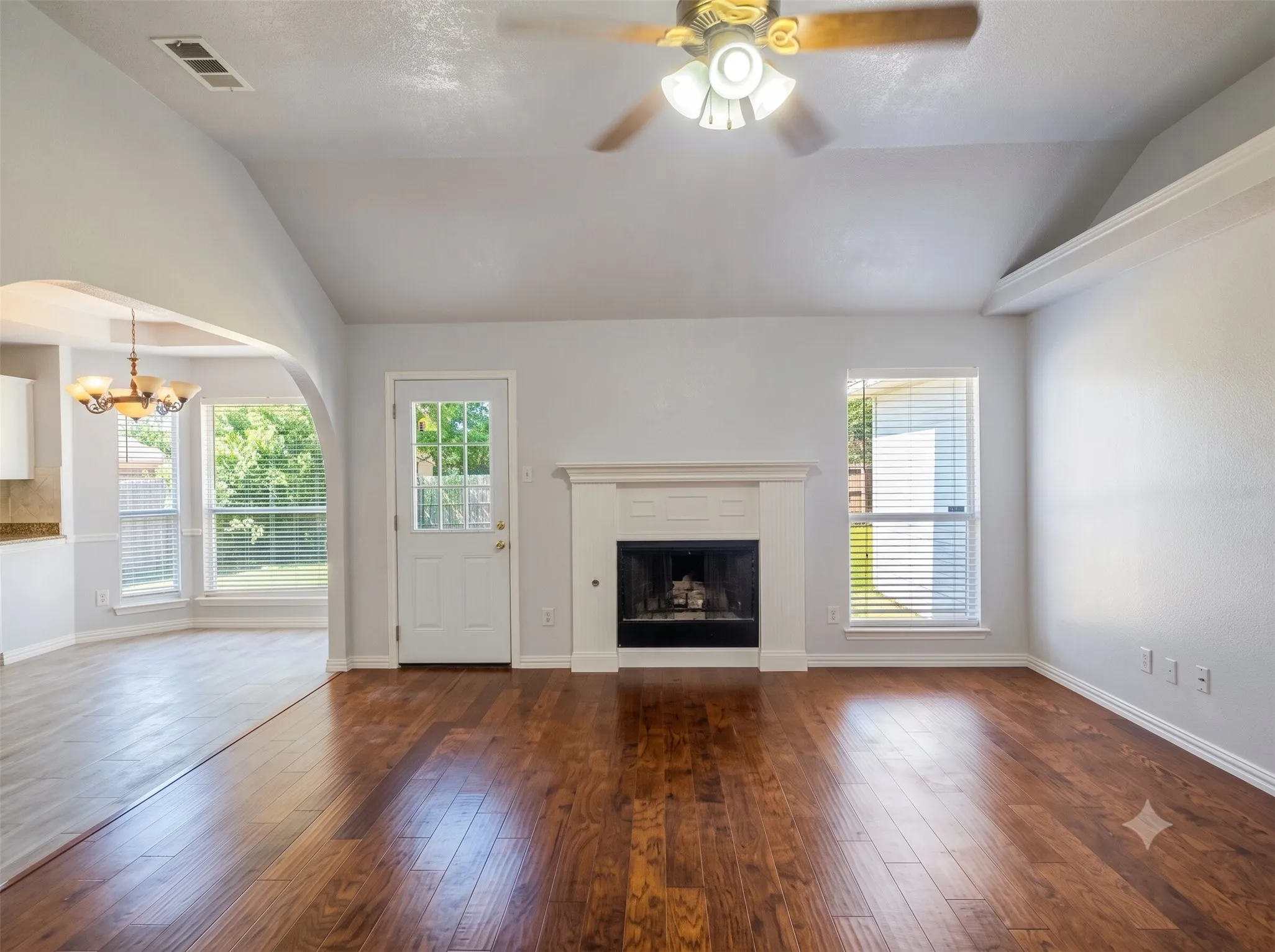 Vaulted ceiling featuring a ceiling fan with integrated lighting, wood-finish flooring, and a fireplace with a white mantel