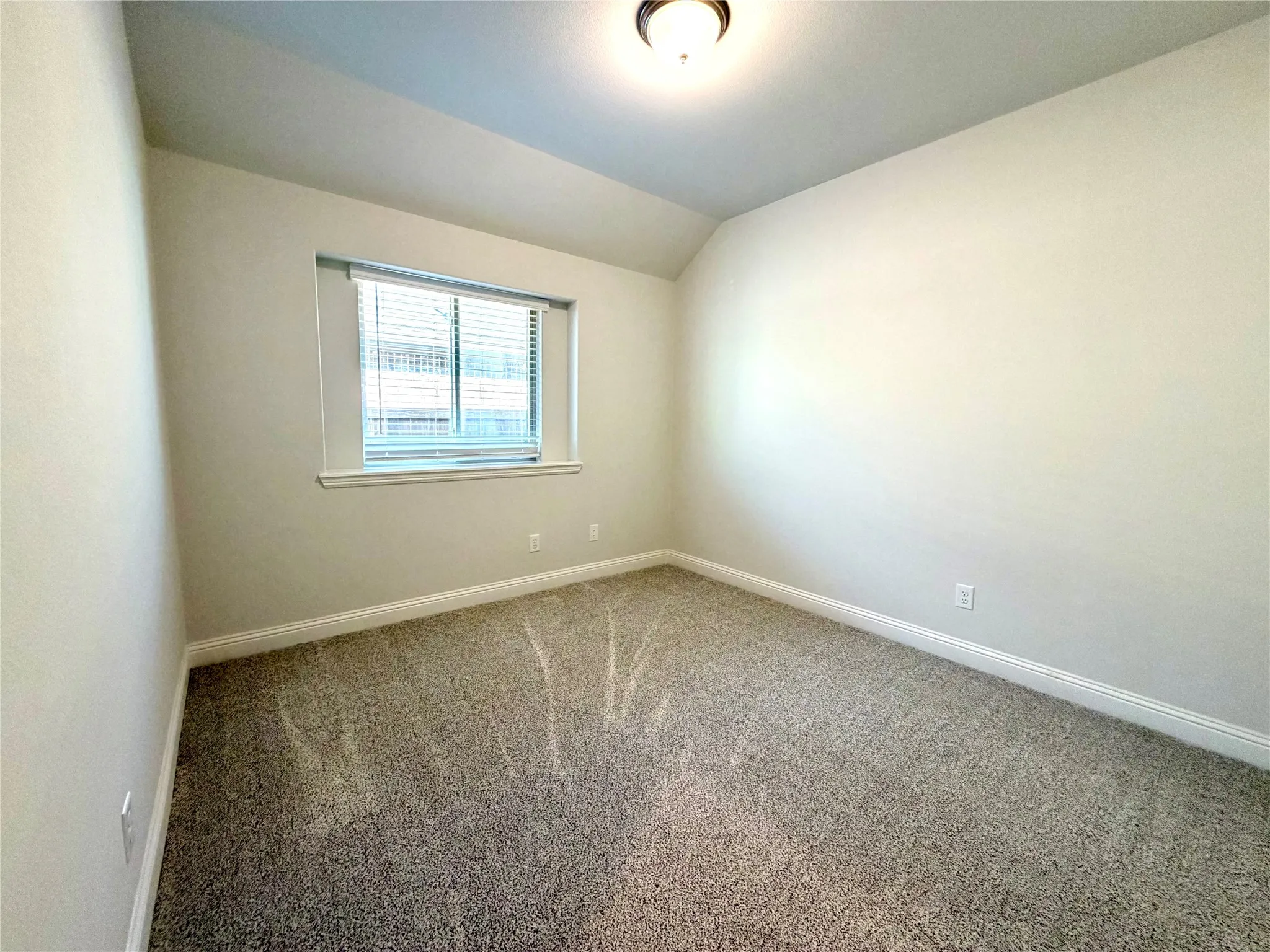 This other secondary bedroom features a calming, neutral-toned color palette on the walls, complemented by plush, high-quality textured carpeting throughout. The room is equipped with functional window blinds for light control and privacy, while the space is illuminated by a clean, modern flush mount ceiling light, creating a bright and inviting atmosphere perfect for guests or family members.