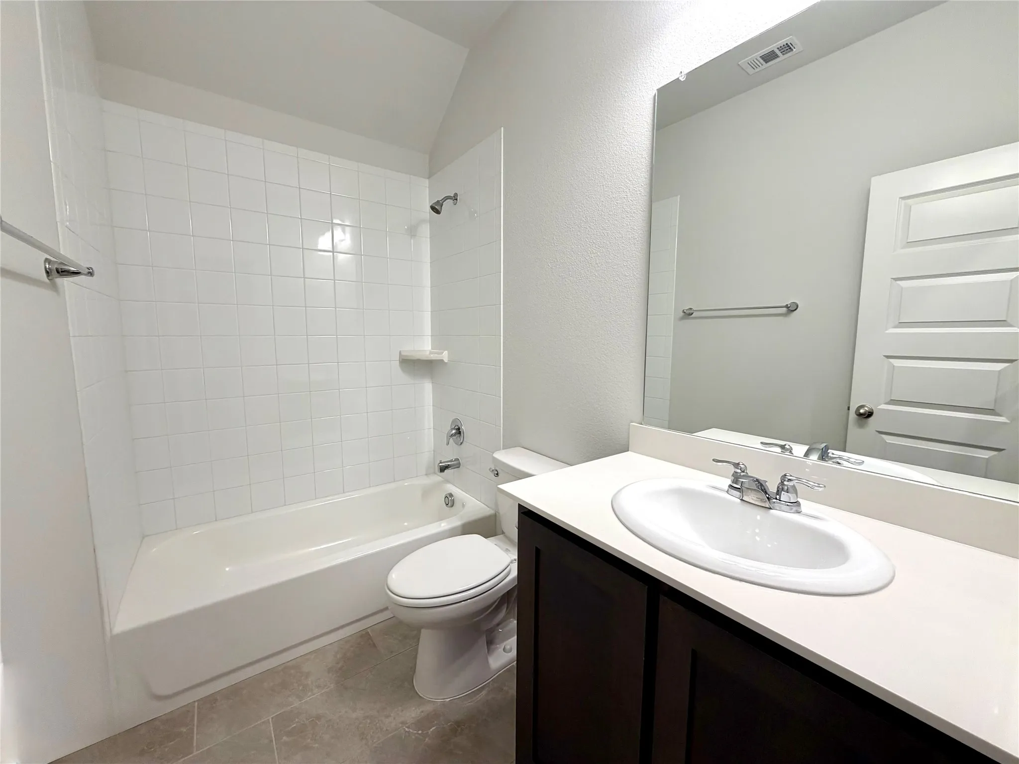 This full guest bathroom showcases a clean and modern design, featuring a classic white bathtub complete with a stylish subway tile surround and a convenient built-in recessed shelf. The space is anchored by an elegant dark wood-finish vanity topped with a crisp white countertop, perfectly complemented by high-quality tiled flooring that adds both durability and visual appeal to the room.
