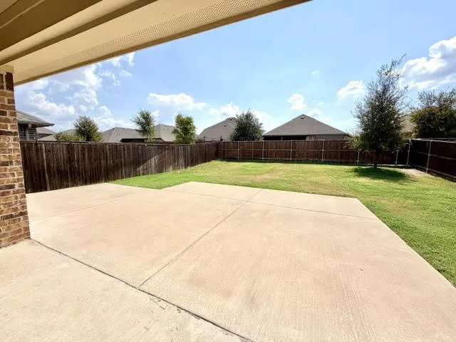 Covered patio with a concrete surface, brick wall, and expansive lawn surrounded by a privacy fence