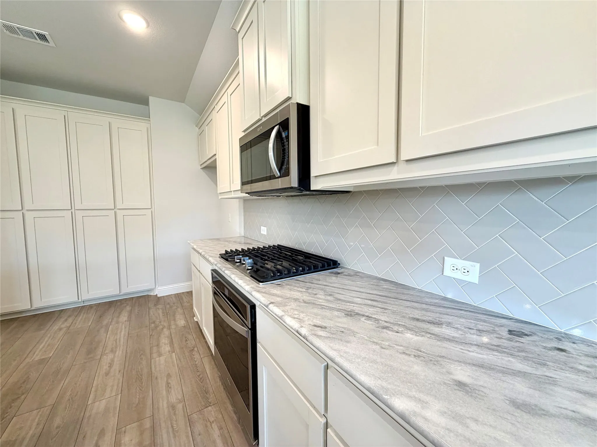 This gourmet kitchen features a high-performance gas cooktop perfect for precision cooking, complemented by a convenient separate oven below for efficient meal preparation. The area includes a sleek, over-the-range vented microwave for optimal ventilation and offers an abundance of sprawling counter space, making it an ideal environment for both culinary enthusiasts and daily entertaining.
