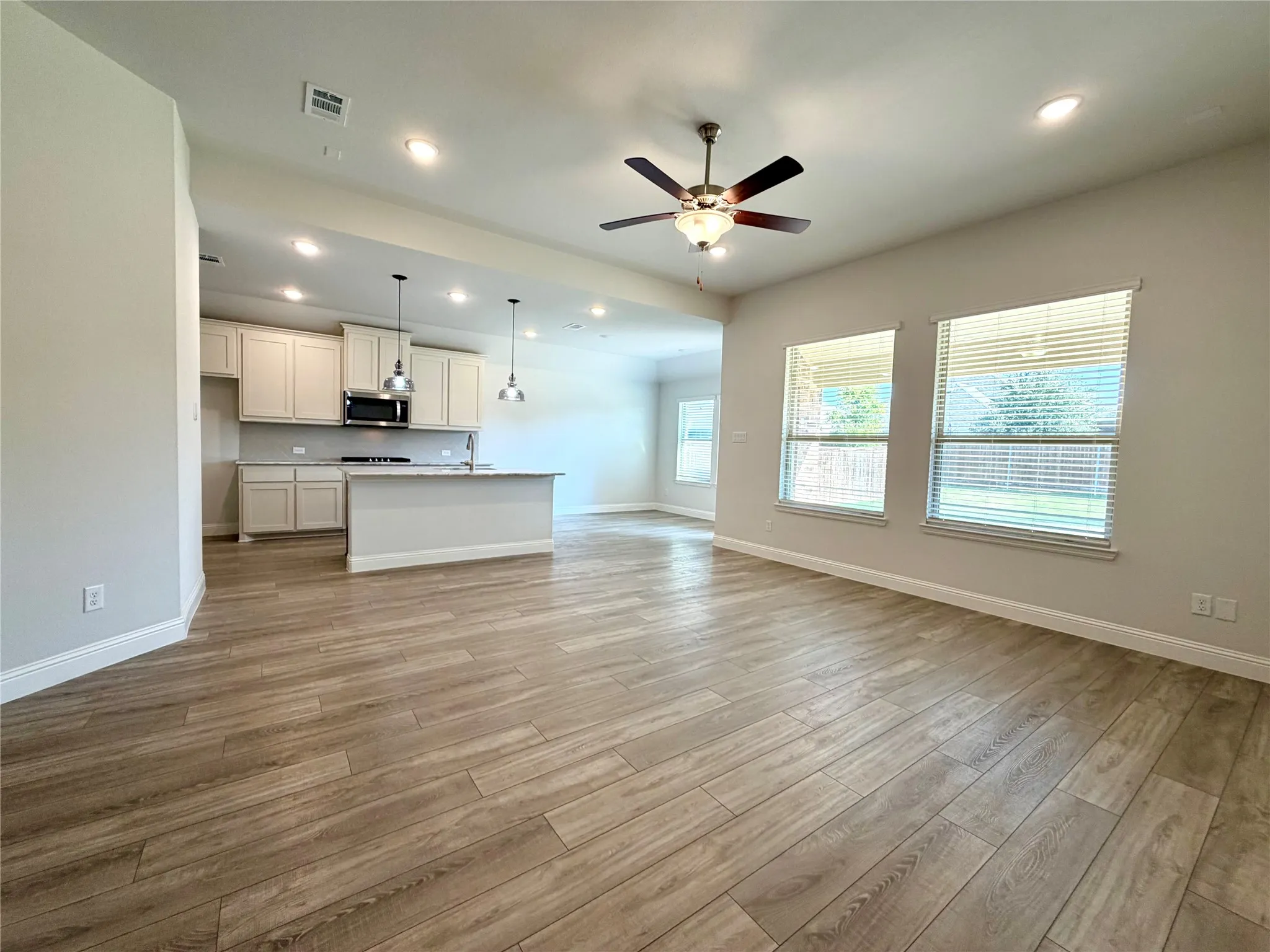 This spacious living room is highlighted by premium luxury vinyl plank (LVP) flooring, energy-efficient recessed lighting, and a ceiling fan. The design features an airy, open-concept floor plan that flows seamlessly into the kitchen and dining area, perfectly complemented by a expansive wall of windows that floods the space with abundant natural light.