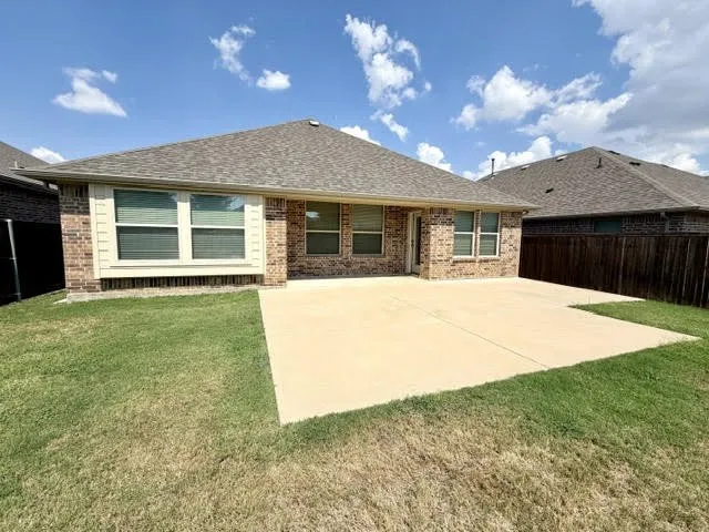 Rear exterior featuring a brick facade, multiple windows, a large concrete patio, and a privacy fence