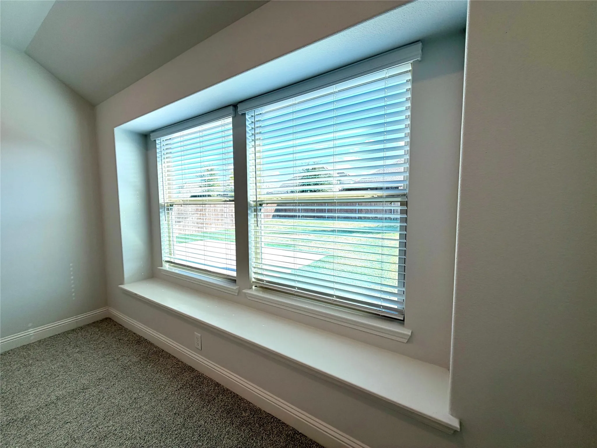 This bright and inviting space features a custom-crafted built-in window seat situated perfectly beneath a pair of large, light-filled windows. The area is framed with clean, crisp white trim that contrasts beautifully with the neutral walls, and the windows are outfitted with high-quality, adjustable custom blinds that allow for effortless control of natural light throughout the day.