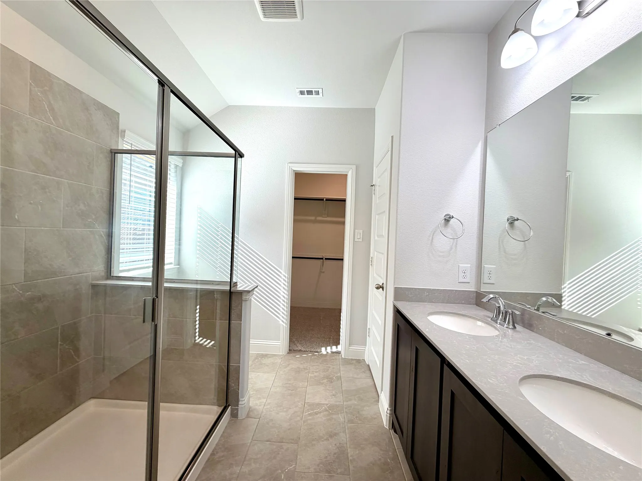 This primary bathroom features a spacious, modern walk-in shower finished with a clean clear glass enclosure and elegant, durable tile surround, perfectly complemented by a functional and stylish dual-sink vanity arrangement.