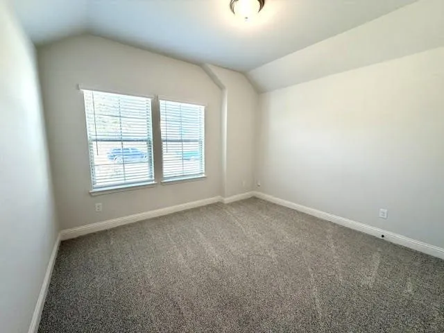 This spacious front secondary bedroom is bathed in natural light, featuring high, airy ceilings and dual windows adorned with sleek blinds. The room is finished with a calming, neutral paint palette and plush wall-to-wall carpet flooring, creating a comfortable and inviting atmosphere perfect for guests or family members.