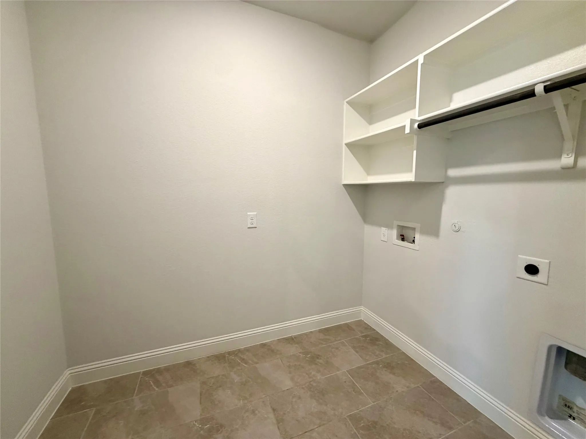 This spacious and highly functional laundry room features durable, easy-to-clean tiled flooring throughout the entire space. It comes fully equipped with convenient built-in shelving units for maximum storage, a sturdy integrated hanging rod for air-drying garments, and significant extra square footage that provides enough room to accommodate an additional refrigerator or freezer.