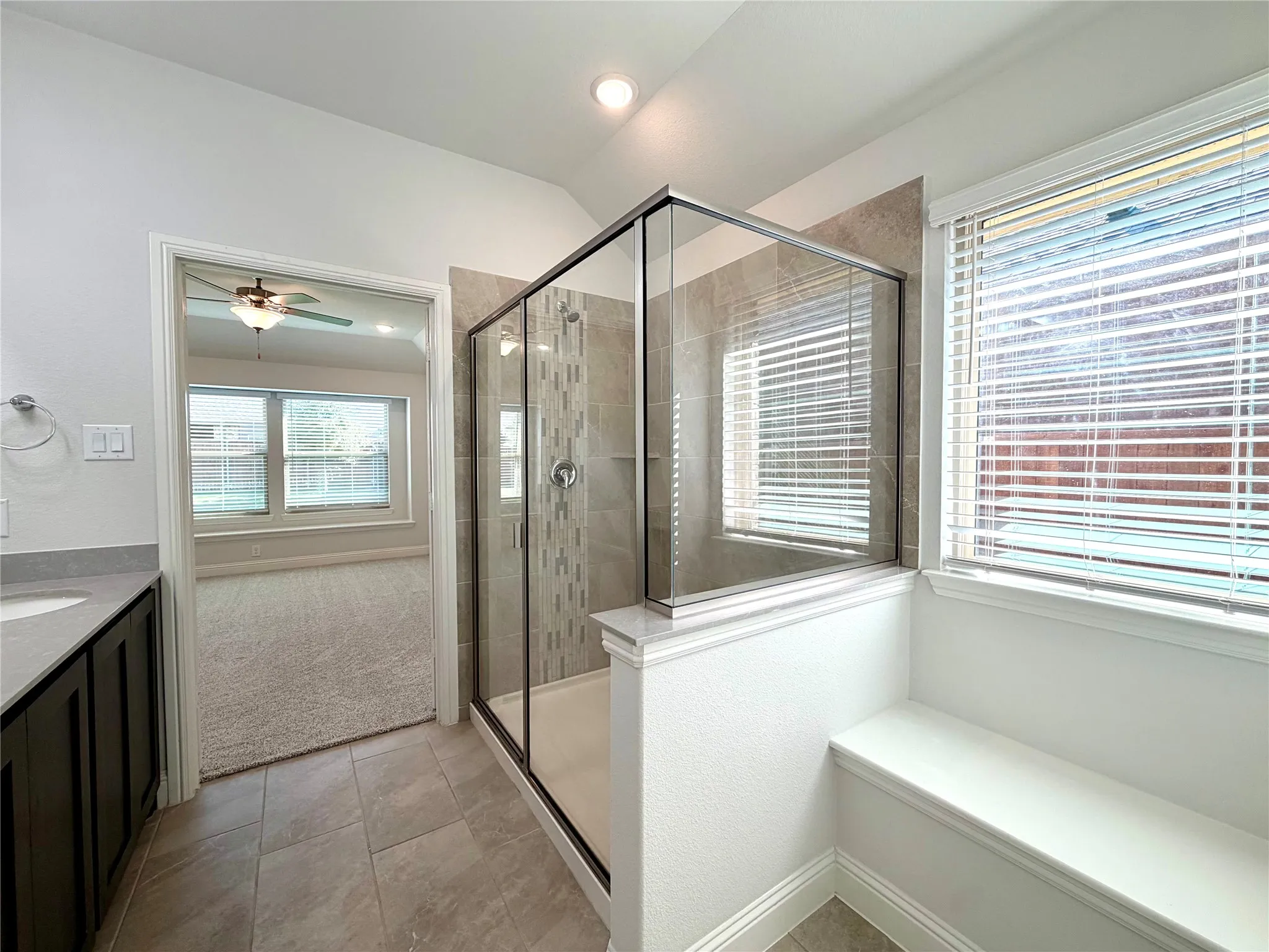 This stunning primary bathroom features a spacious walk-in shower enhanced by a sleek glass enclosure, exquisite custom tile work, and a convenient, beautifully integrated built-in bench for added comfort and functionality.