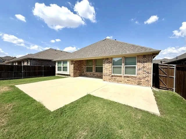 Brick exterior with multiple windows, a large concrete patio, and a wood privacy fence