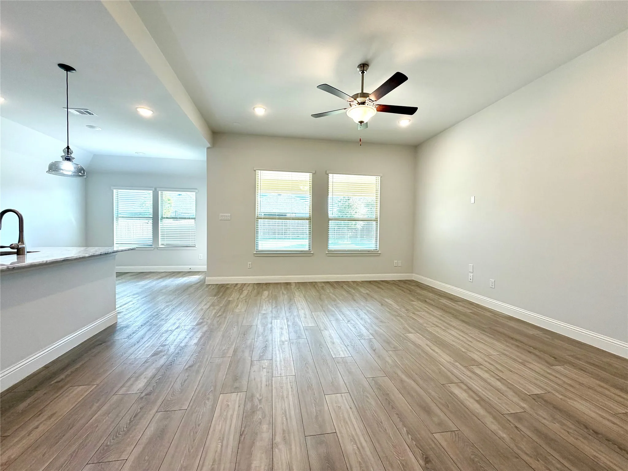 This bright and expansive open-concept living area features a versatile layout that seamlessly connects the main living spaces, highlighted by large windows that provide an inviting, panoramic view of the spacious back yard.