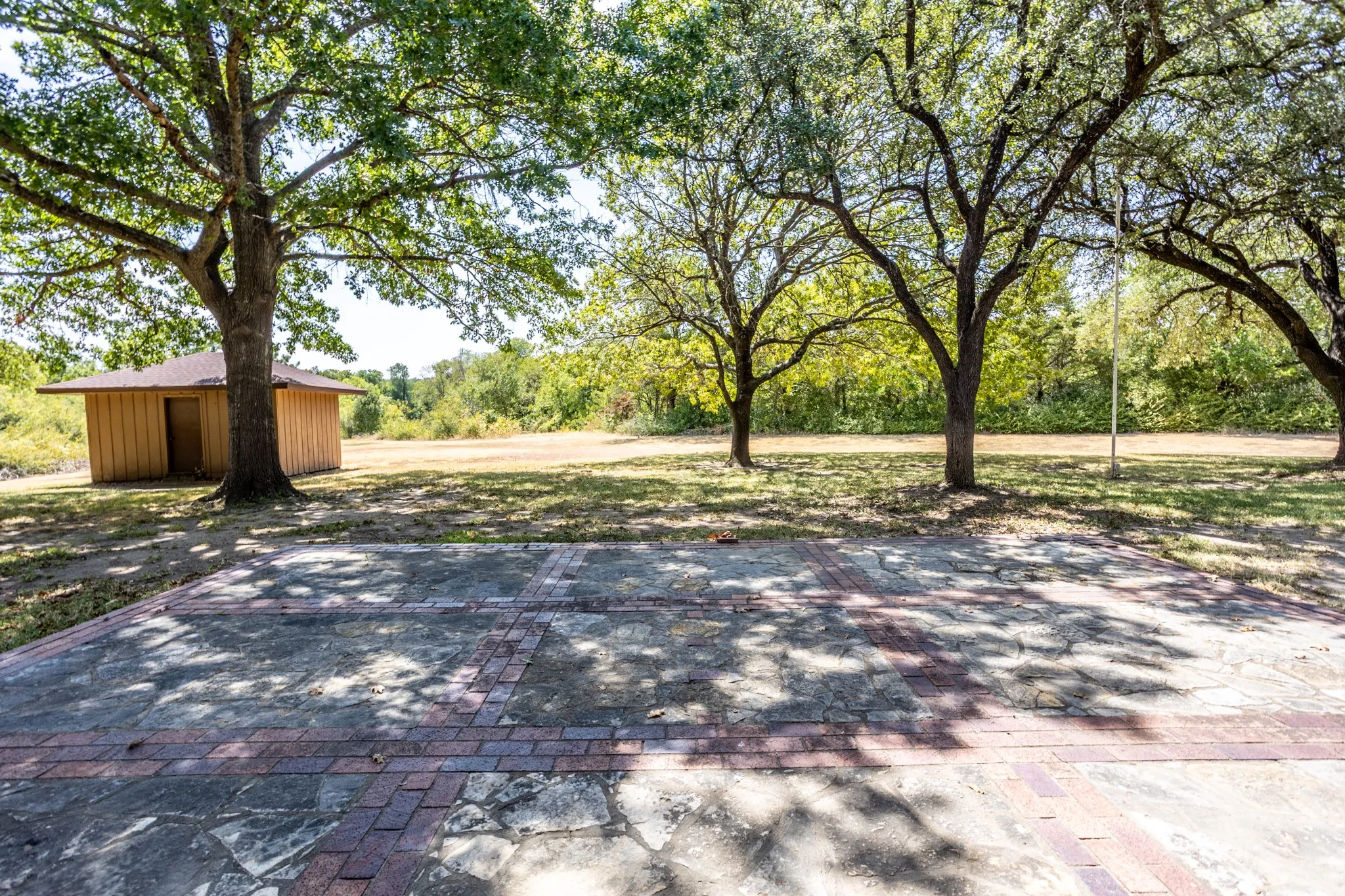 Looking from patio to back area with small storage building.