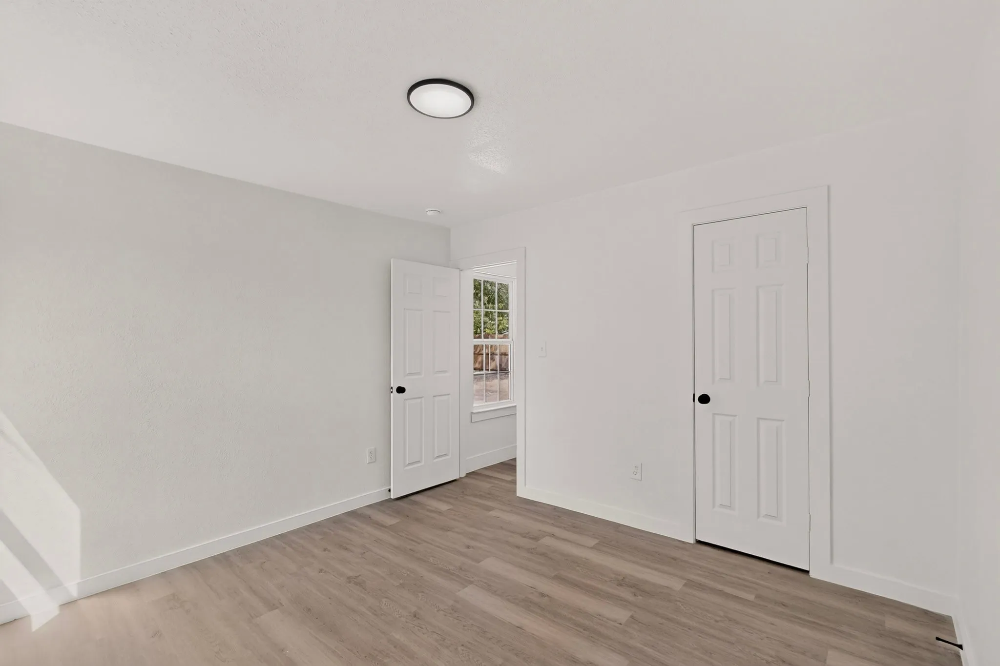 Wood-finish flooring, white walls, and a contemporary flush-mount ceiling light