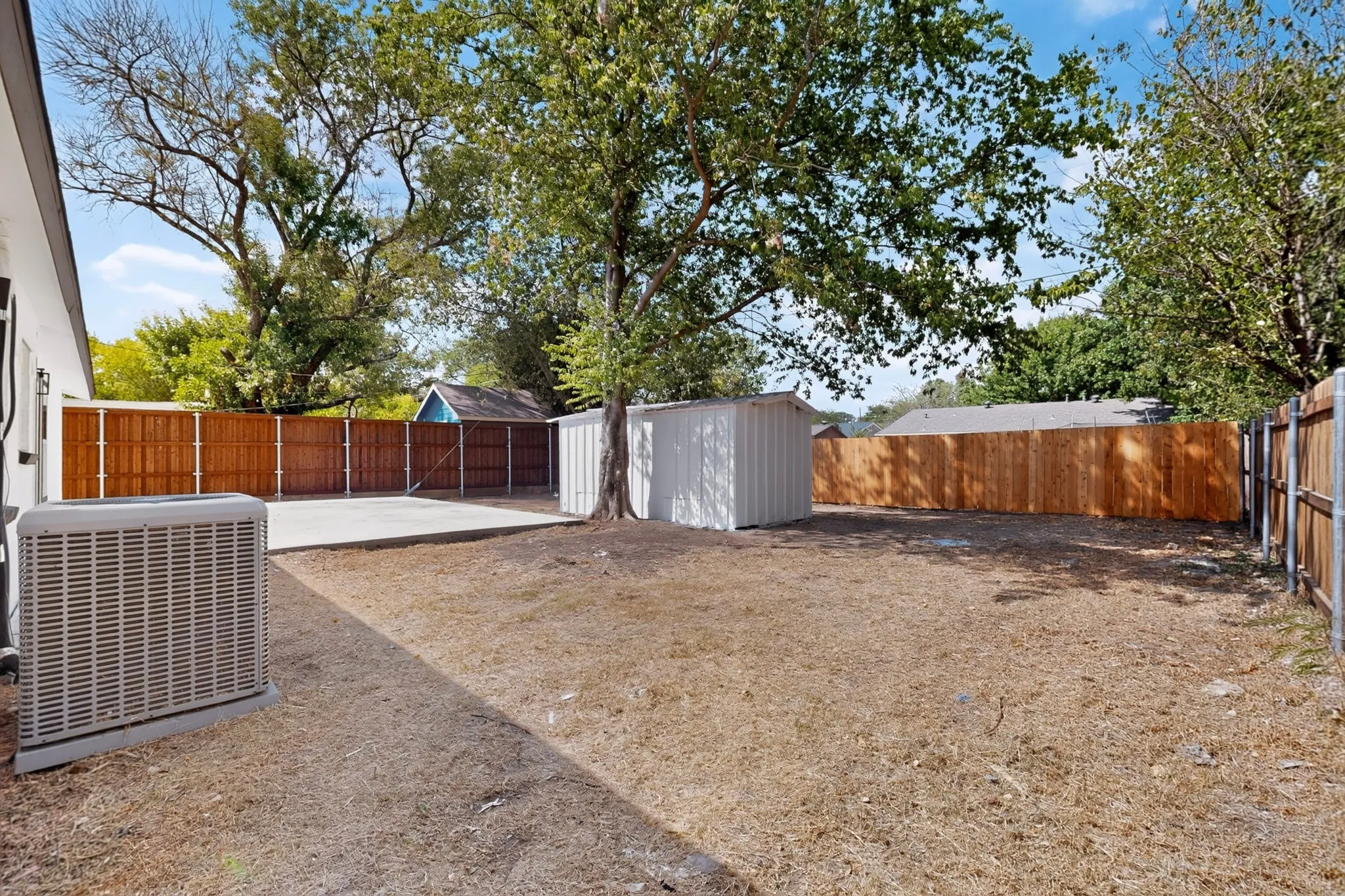 Expansive backyard featuring a concrete patio, wood fencing, and mature trees