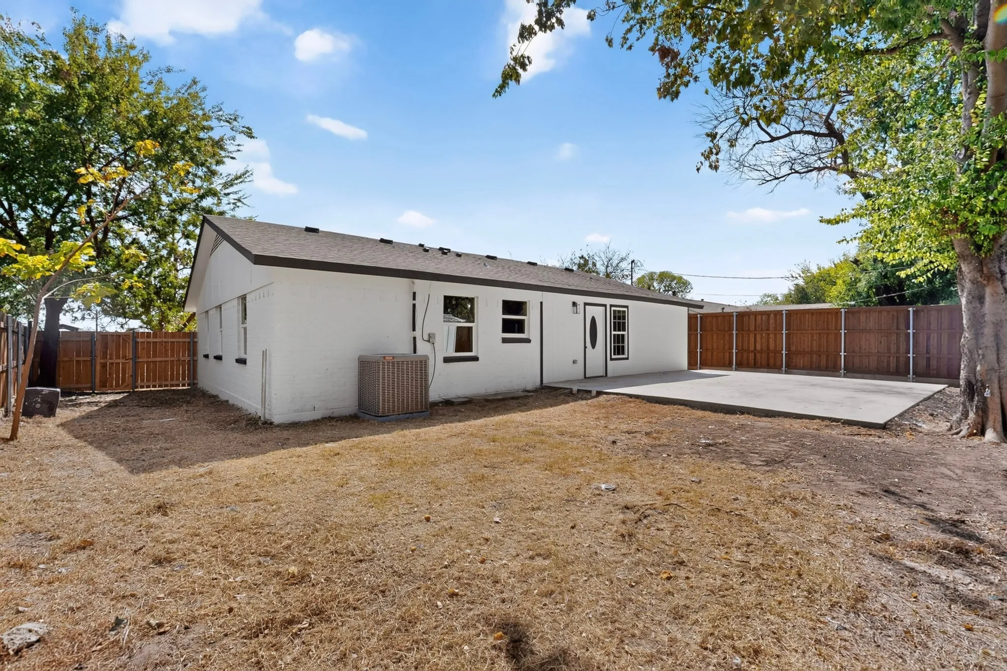 Expansive backyard featuring a concrete patio, wood privacy fencing, and mature trees