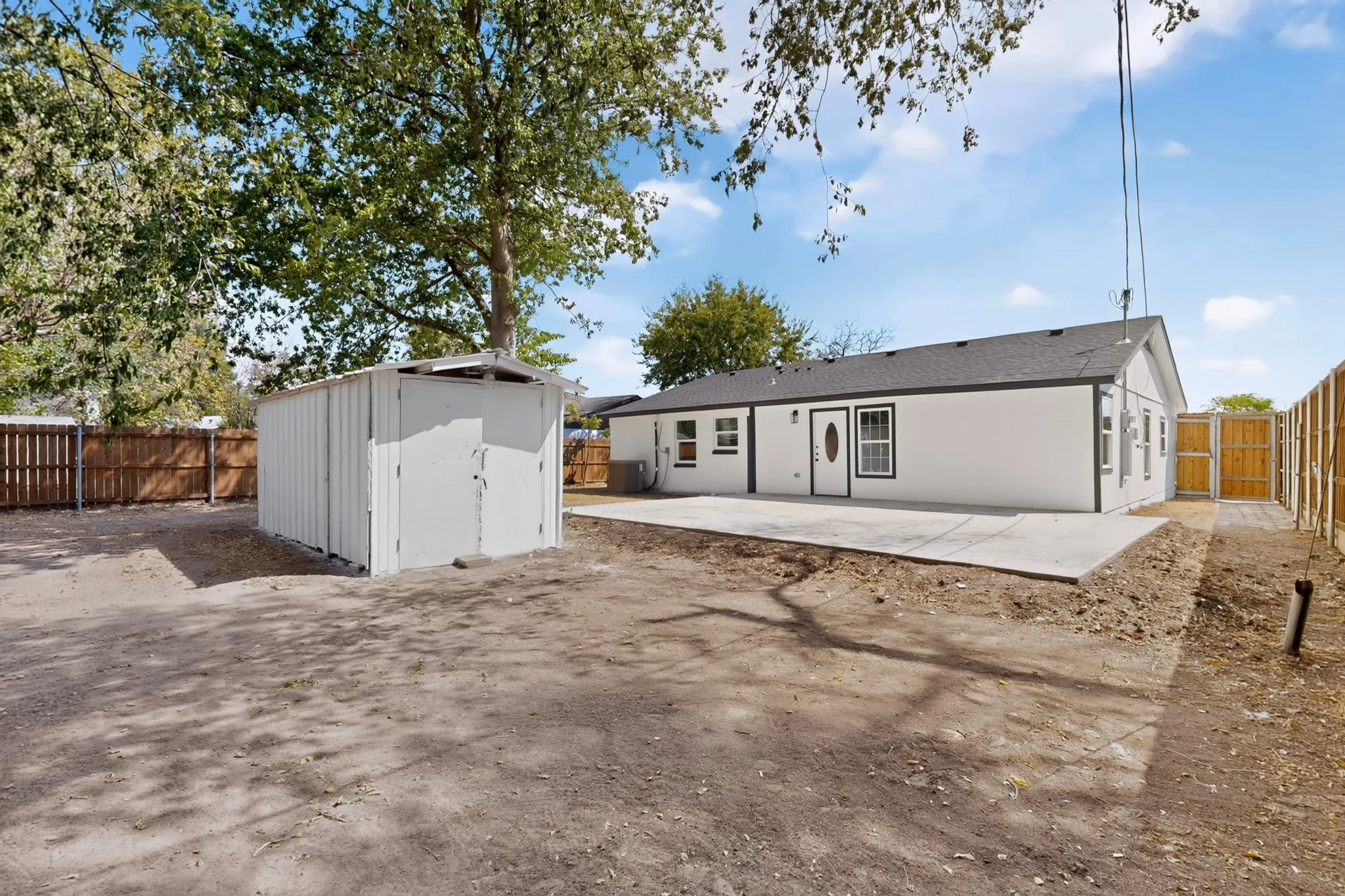 Rear exterior featuring a concrete patio, white painted siding, dark trim windows, and a detached storage shed