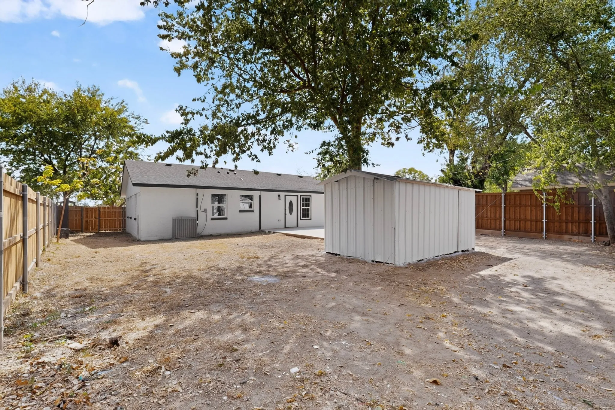 Expansive outdoor space featuring a white structure, mature trees, and a full privacy fence