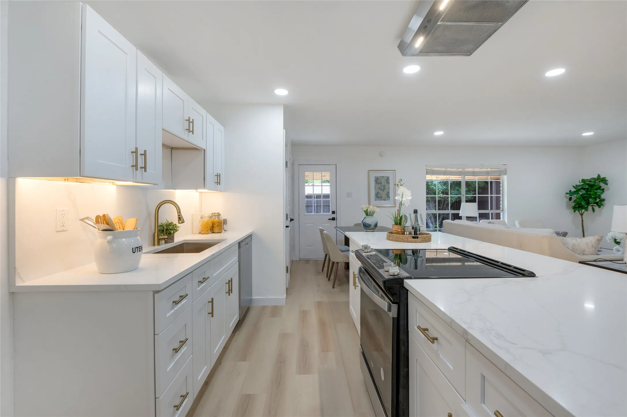 Kitchen featuring white shaker-style cabinetry, a built-in stainless steel dishwasher, a gold-finish gooseneck faucet, a built-in stainless steel oven, and light wood-finish flooring