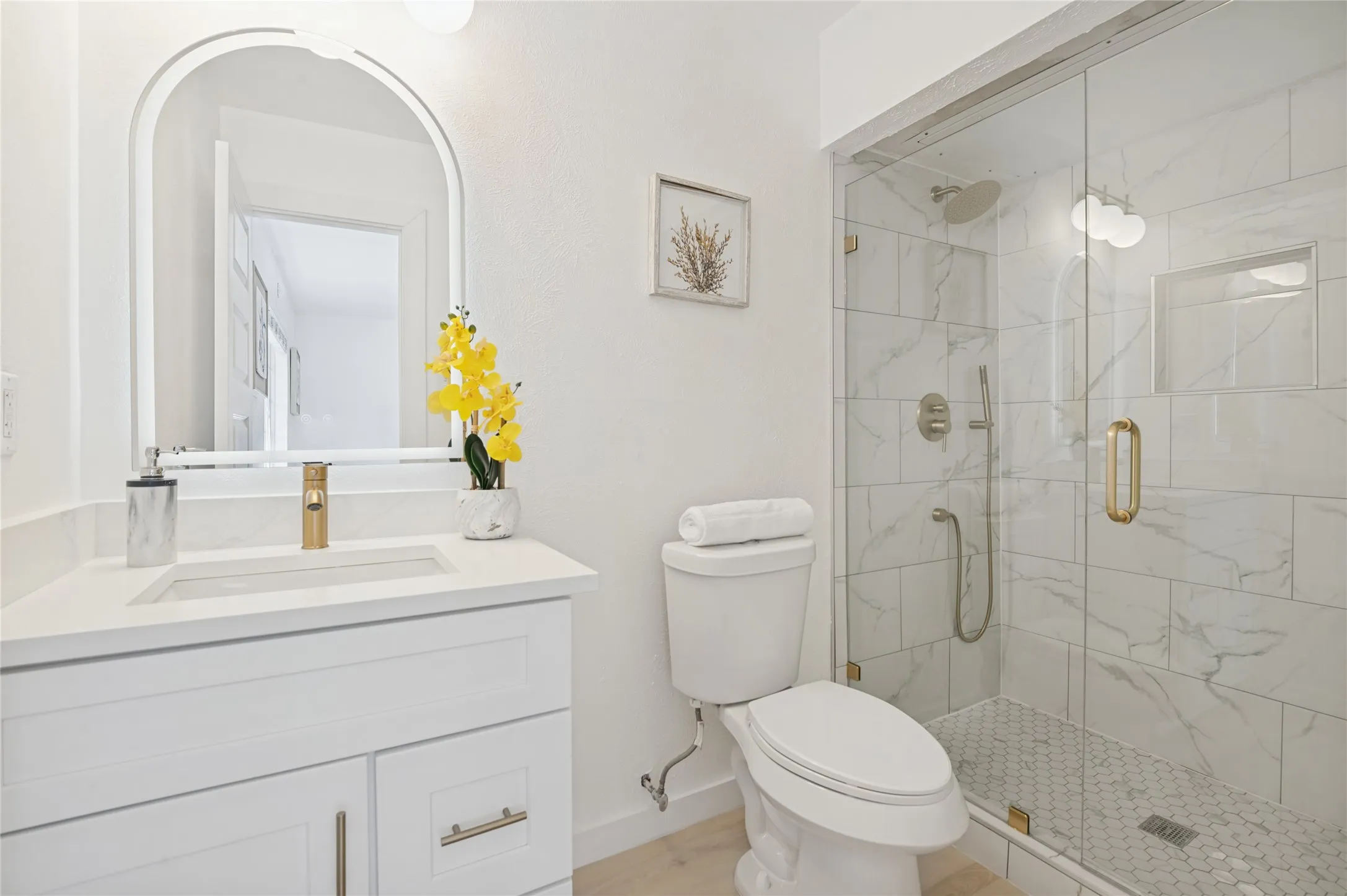 Spa-inspired primary bathroom featuring a floating vanity with white cabinetry, quartz countertop, and chrome fixtures, paired with a frameless glass-enclosed shower with marble-look tile surround and rainfall showerhead