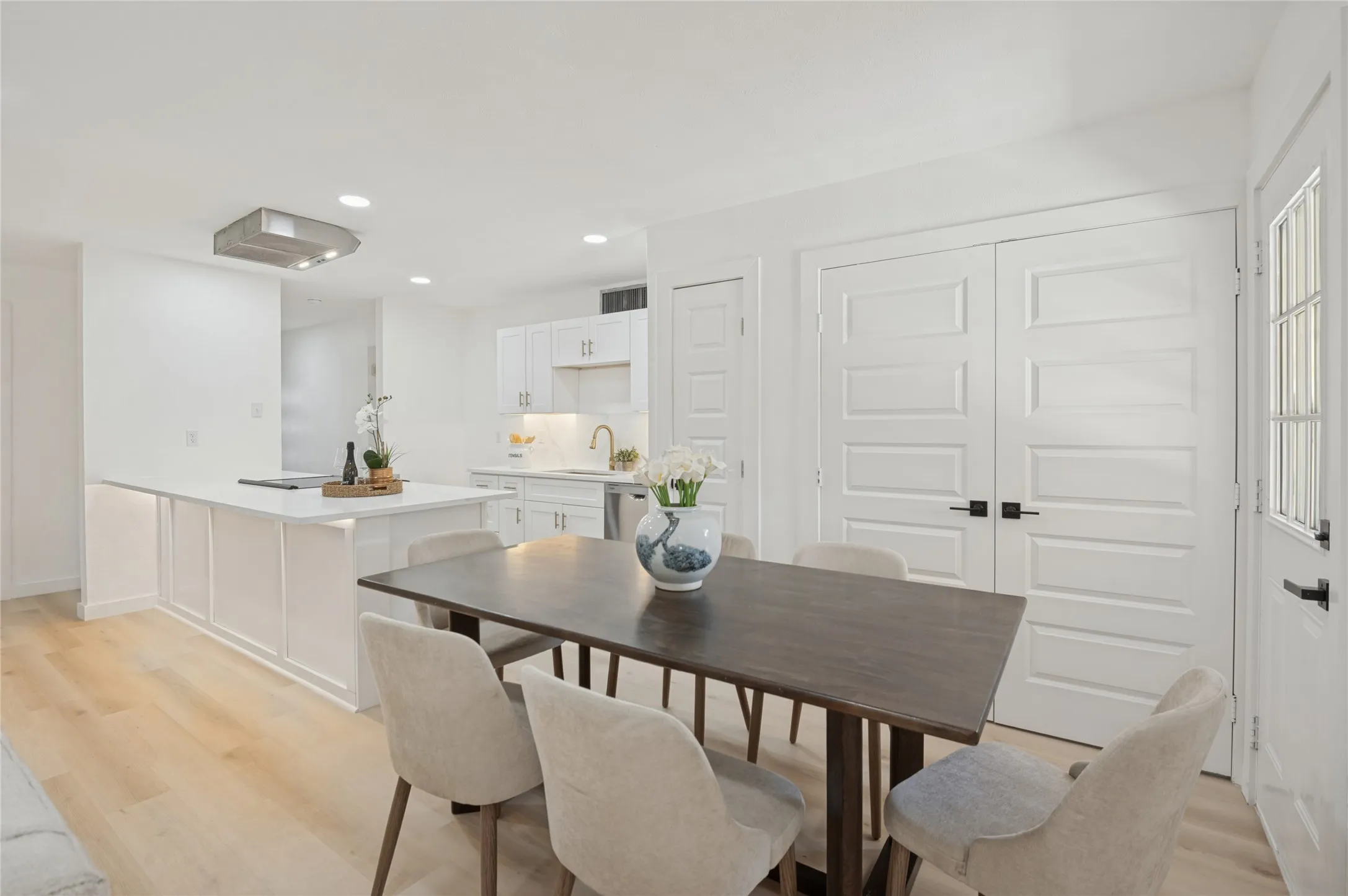 Recessed lighting, wood-finish flooring, white paneled doors, white kitchen cabinetry, and a kitchen island with a cooktop