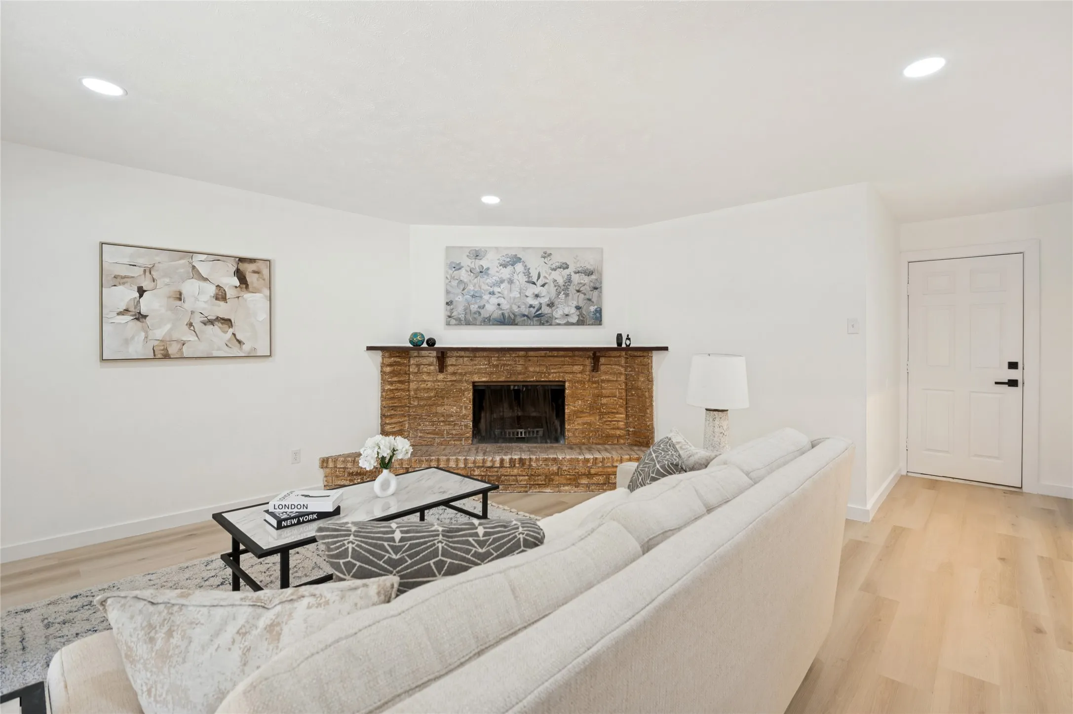 Brick fireplace with a dark wood mantel, recessed lighting, and light wood-finish flooring