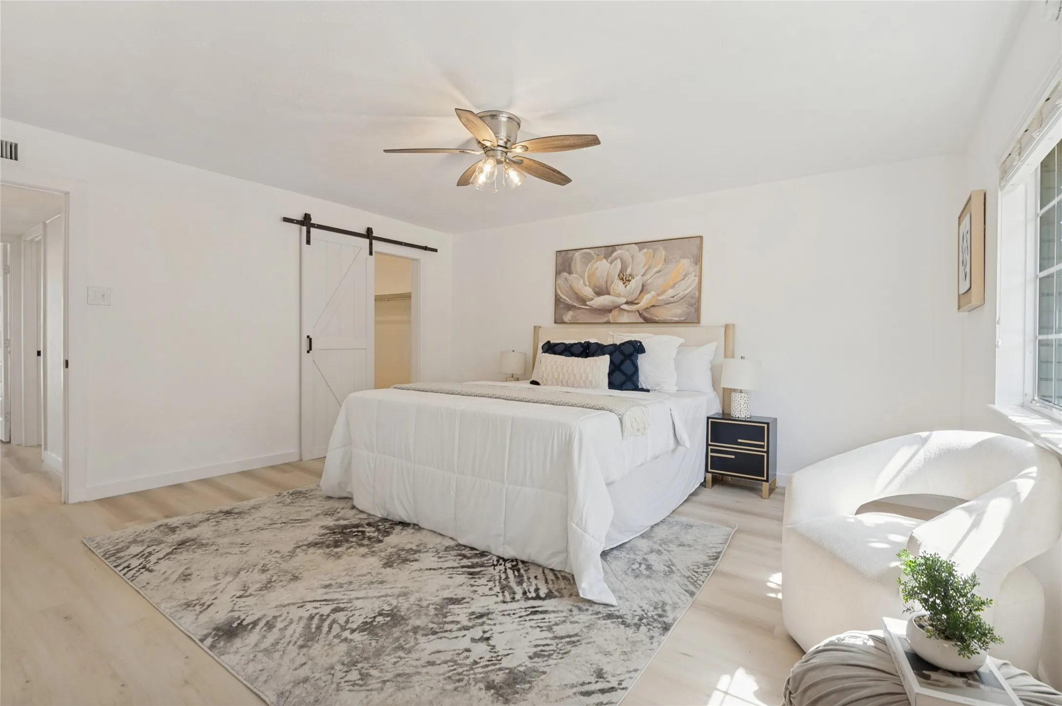 Wood-finish flooring, ceiling fan with integrated lighting, sliding barn door, and a window with horizontal blinds
