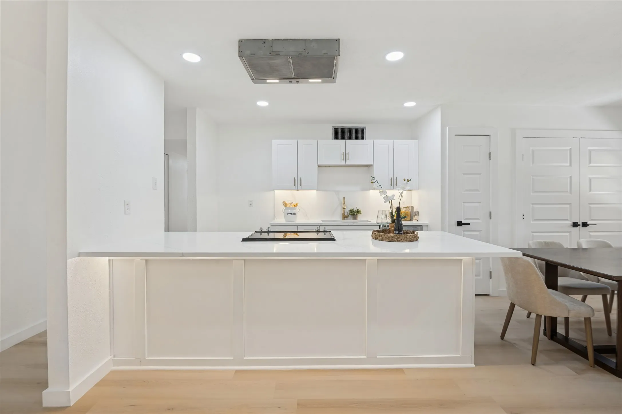 Open-concept kitchen with a large island, white cabinetry, integrated cooktop, and wood-finish flooring