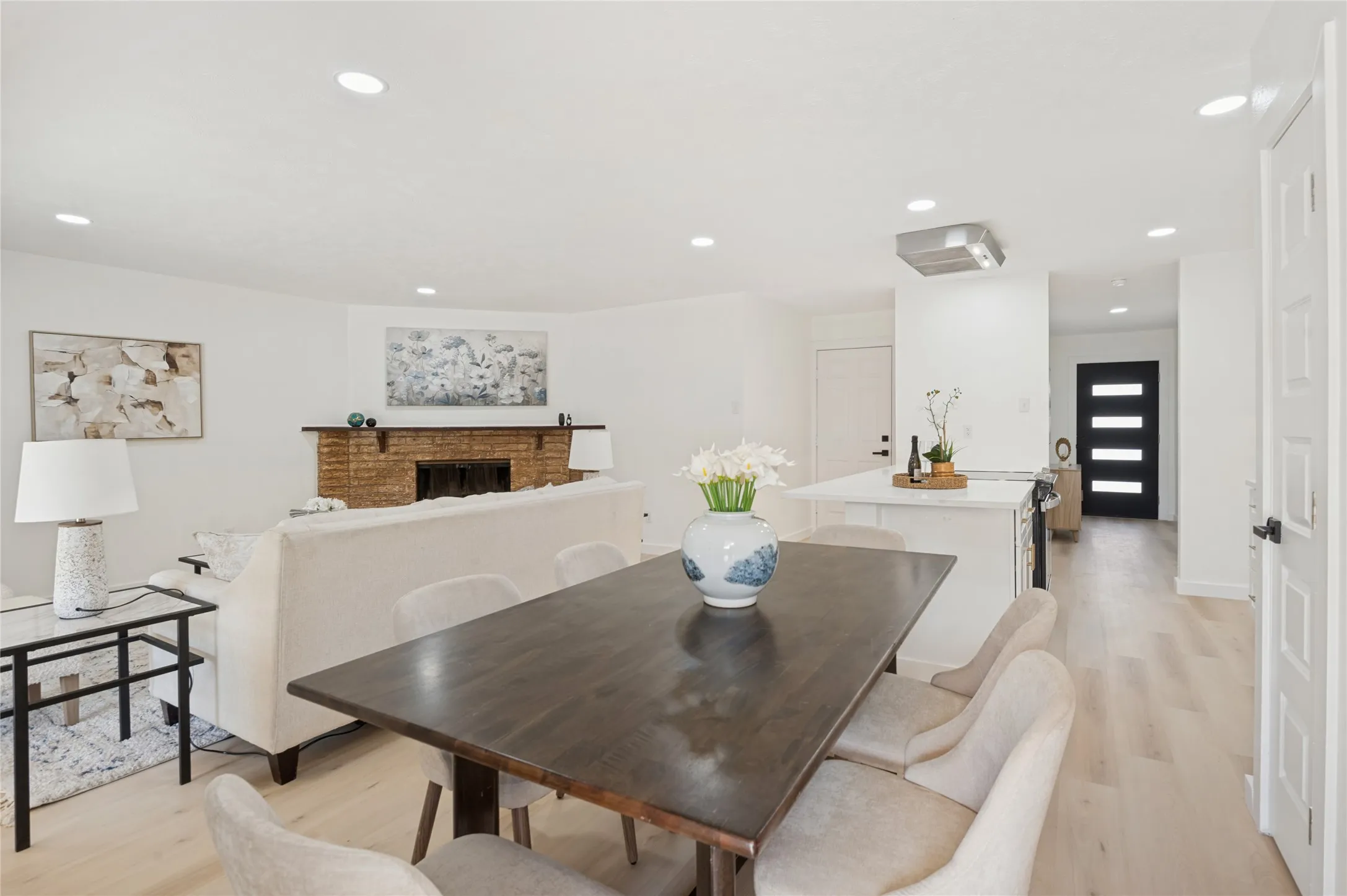 Recessed lighting, wood-finish flooring, brick fireplace, kitchen island with counter seating, and a modern paneled entry door
