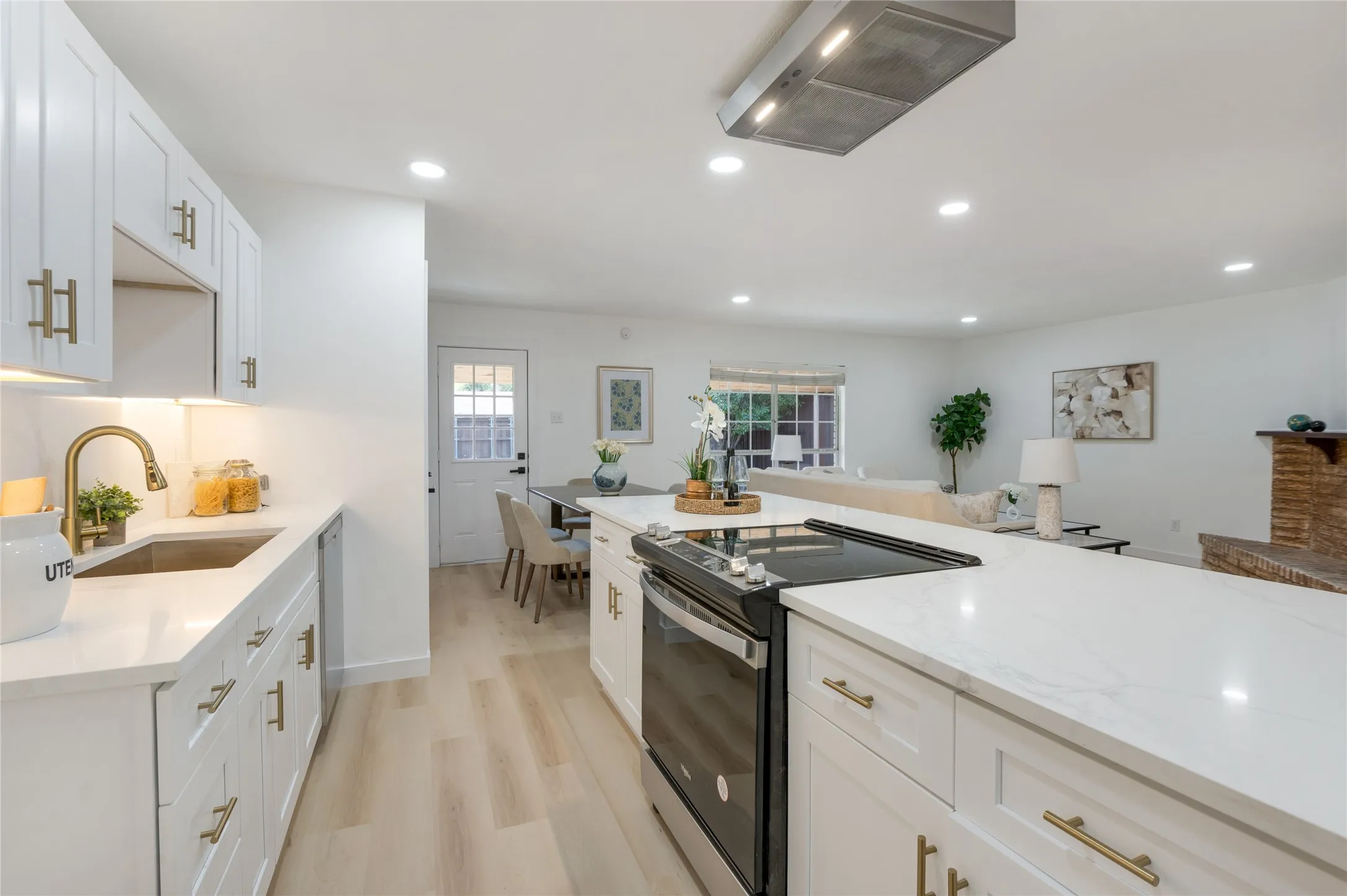 White cabinetry with gold-finish hardware, stainless steel sink, and light-tone wood-finish flooring
