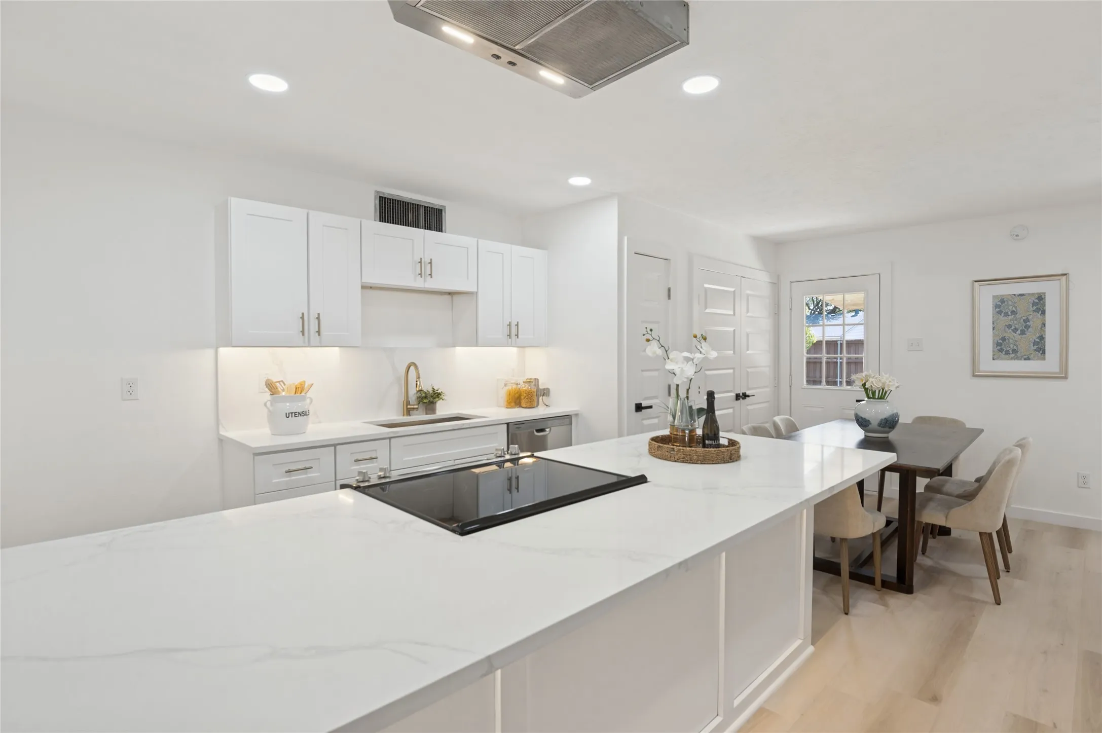 Kitchen featuring an expansive island with a built-in cooktop, white shaker cabinetry, gold-finish hardware, and a single-basin sink with a gold-finish faucet