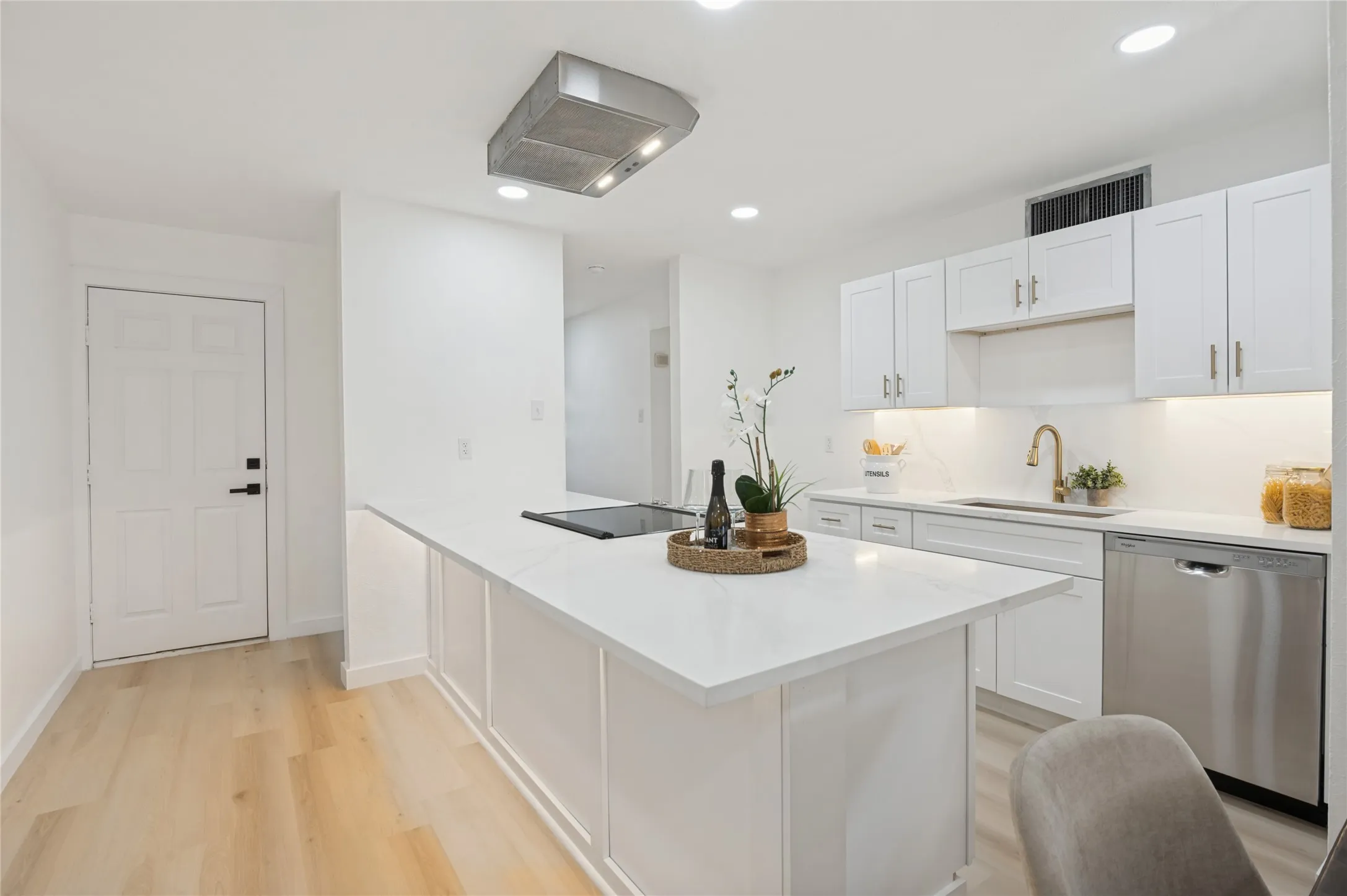 Modern kitchen featuring white cabinetry, a large center island with a cooktop, stone countertops, stainless steel appliances, and wood-finish flooring