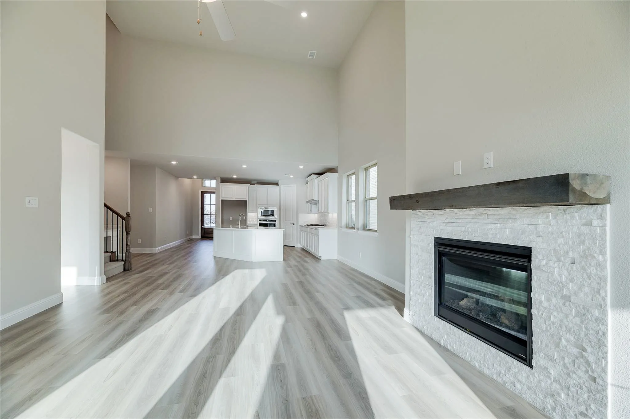 Vaulted ceiling, wood-finish flooring, white stack stone fireplace surround, dark wood mantel, and recessed lighting