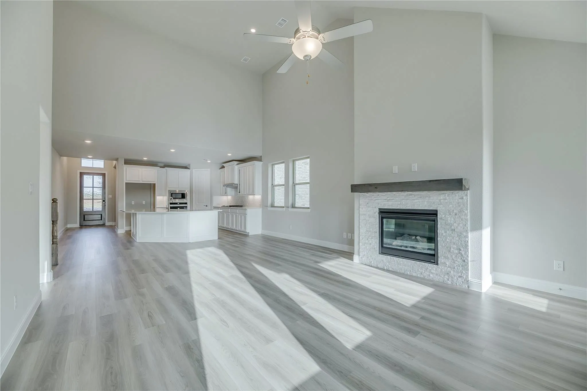 Vaulted ceilings, wood-finish flooring, white stone fireplace, and a white kitchen with a central island and built-in appliances