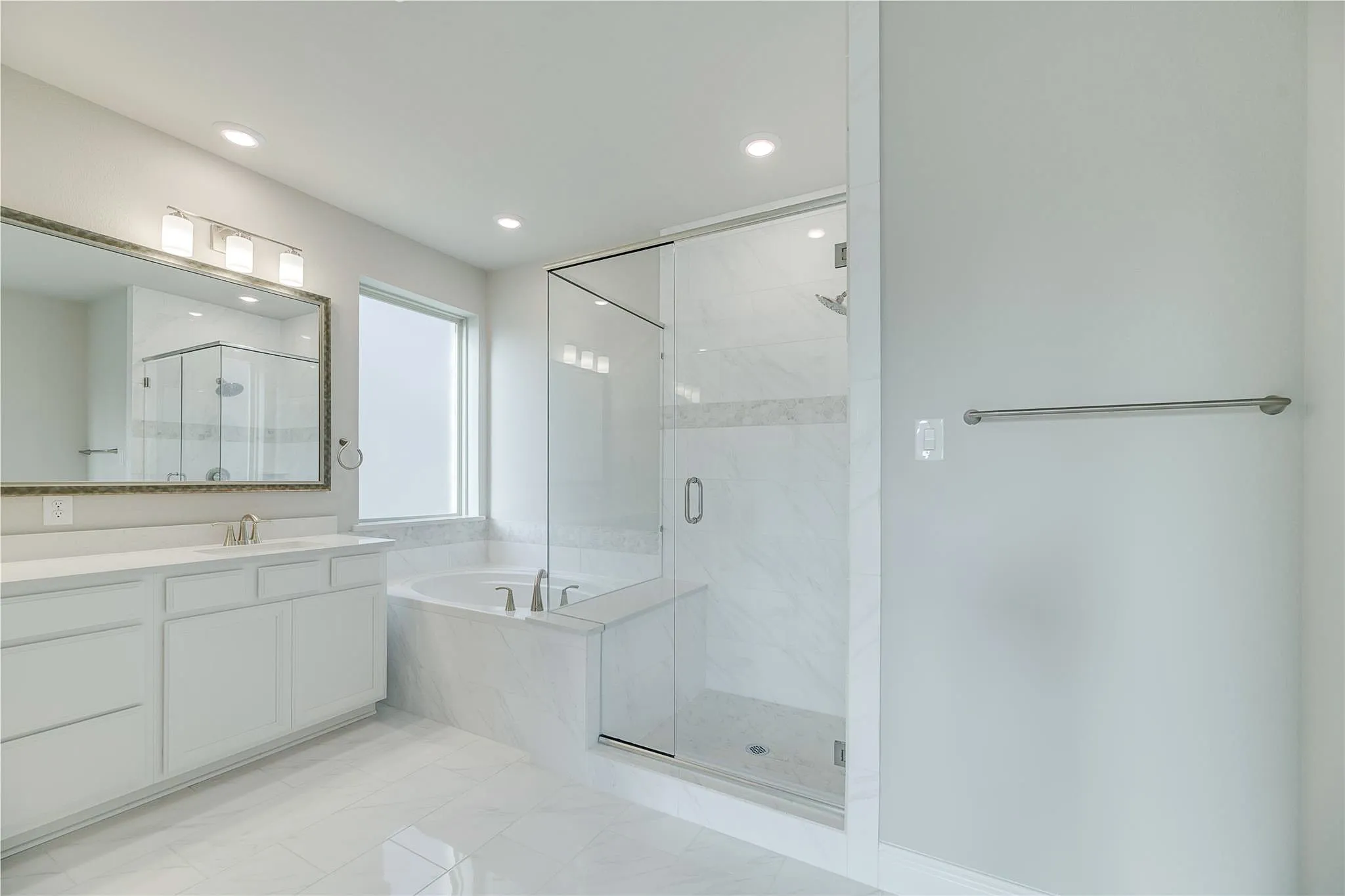 White vanity with ample storage, large framed mirror, recessed lighting, glass-enclosed shower, and built-in tub