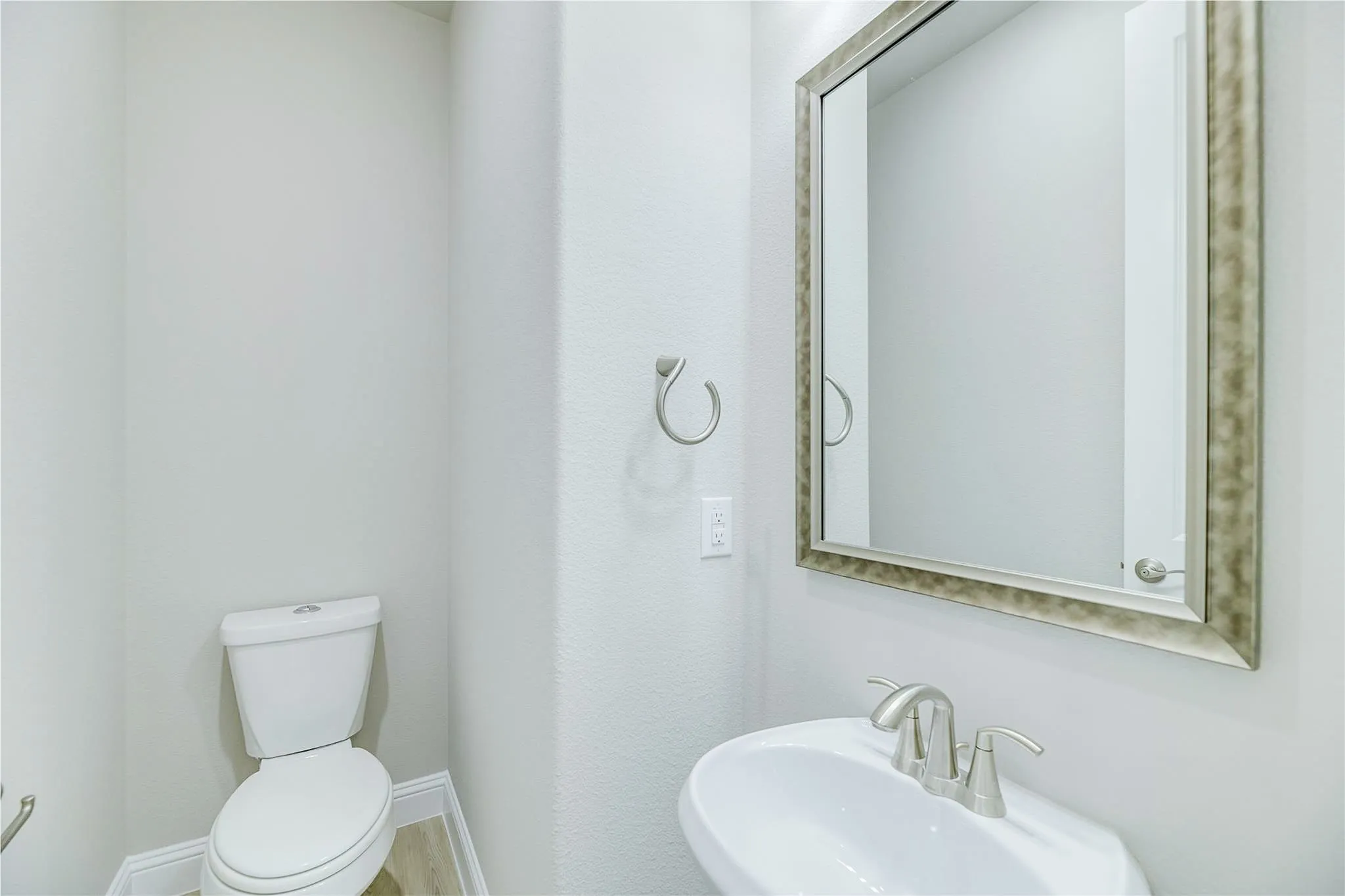 Pedestal sink with brushed nickel faucet, framed mirror, and light wood-finish​​‌​​​​‌​​‌‌​‌‌​​​‌‌​‌​‌​‌​​​‌​​ flooring