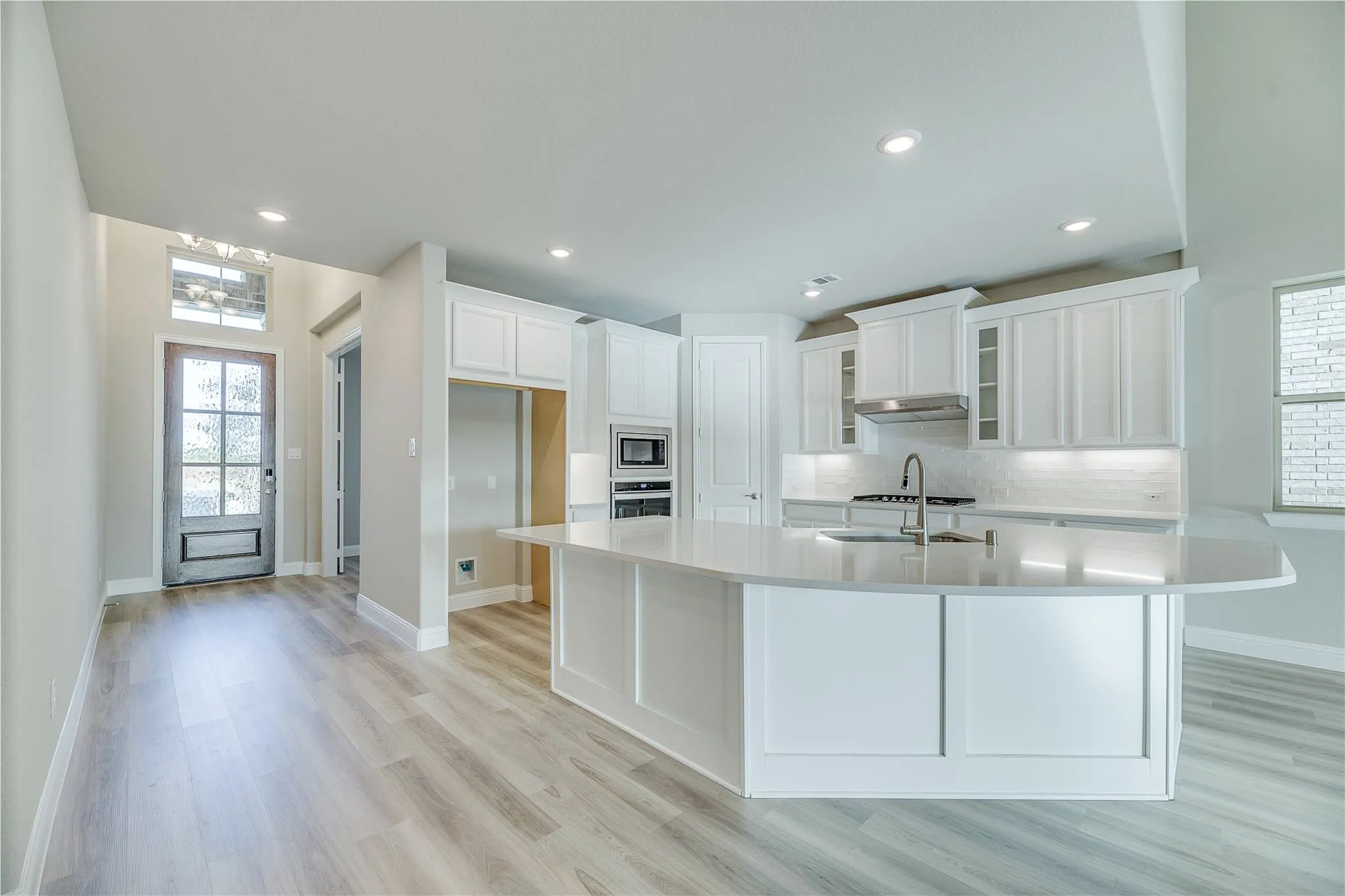 White cabinetry, light wood-finish flooring, recessed lighting, double wall oven, and a built-in microwave