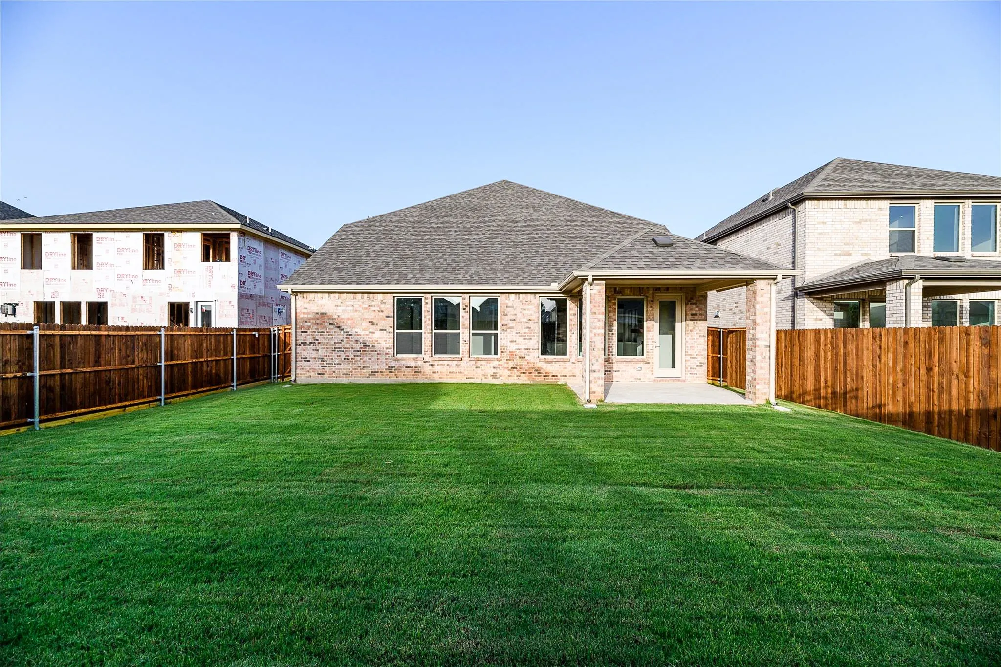 Expansive backyard featuring a manicured lawn, wood fencing, covered patio, and brick exterior