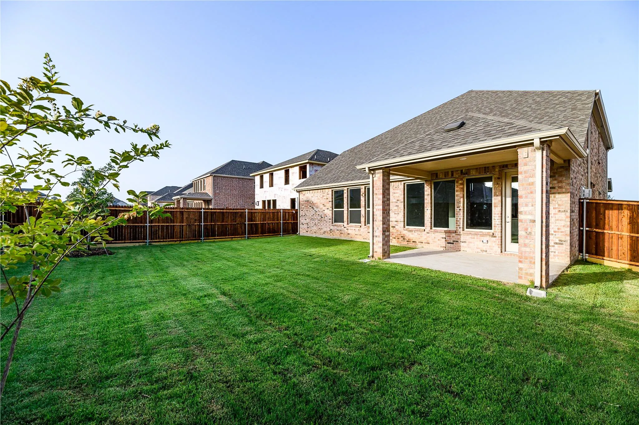 Expansive backyard with a covered patio, brick exterior, multiple windows, and a wood privacy fence