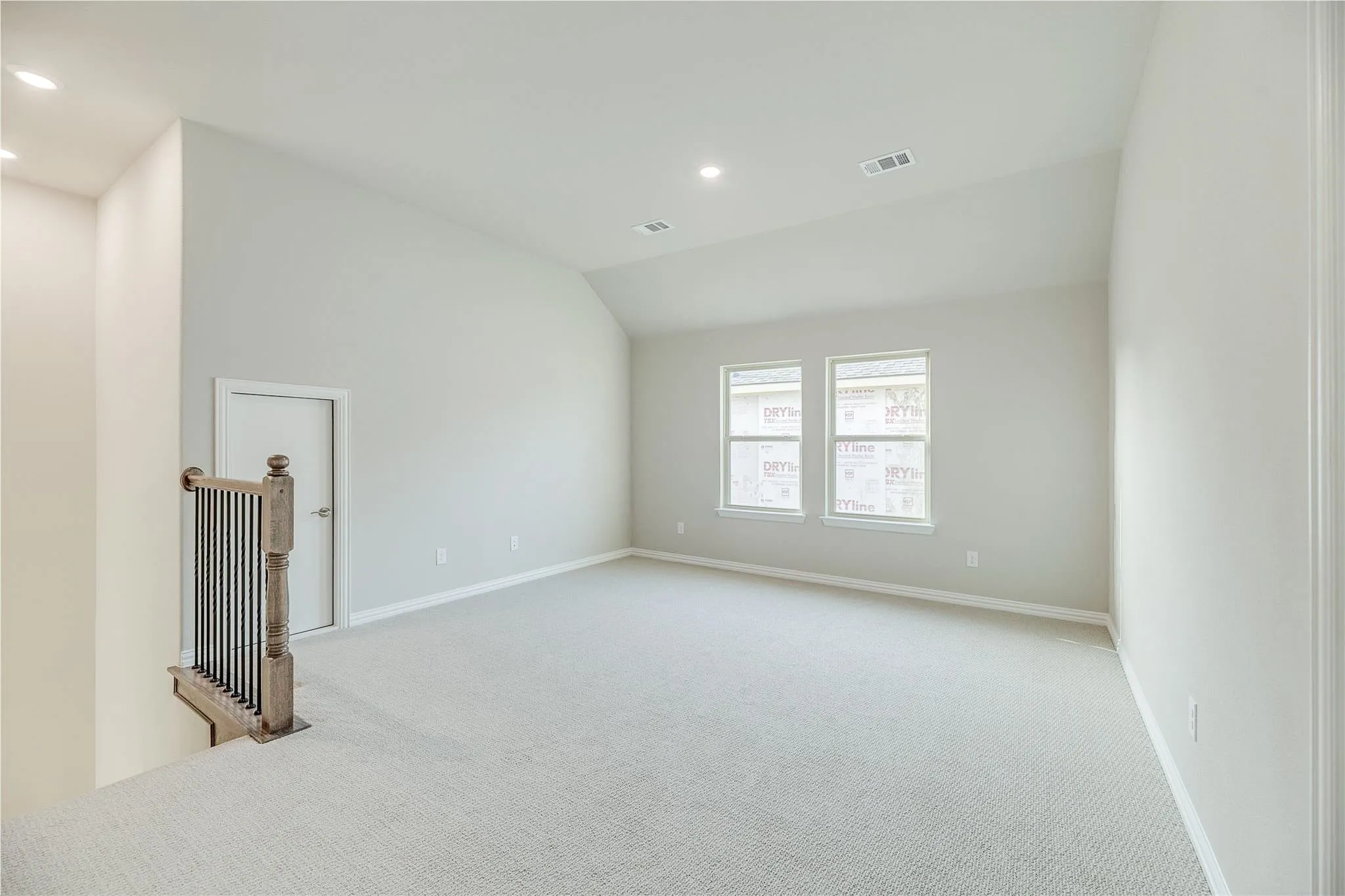 Spacious carpeted area featuring a vaulted ceiling, recessed lighting, and two windows